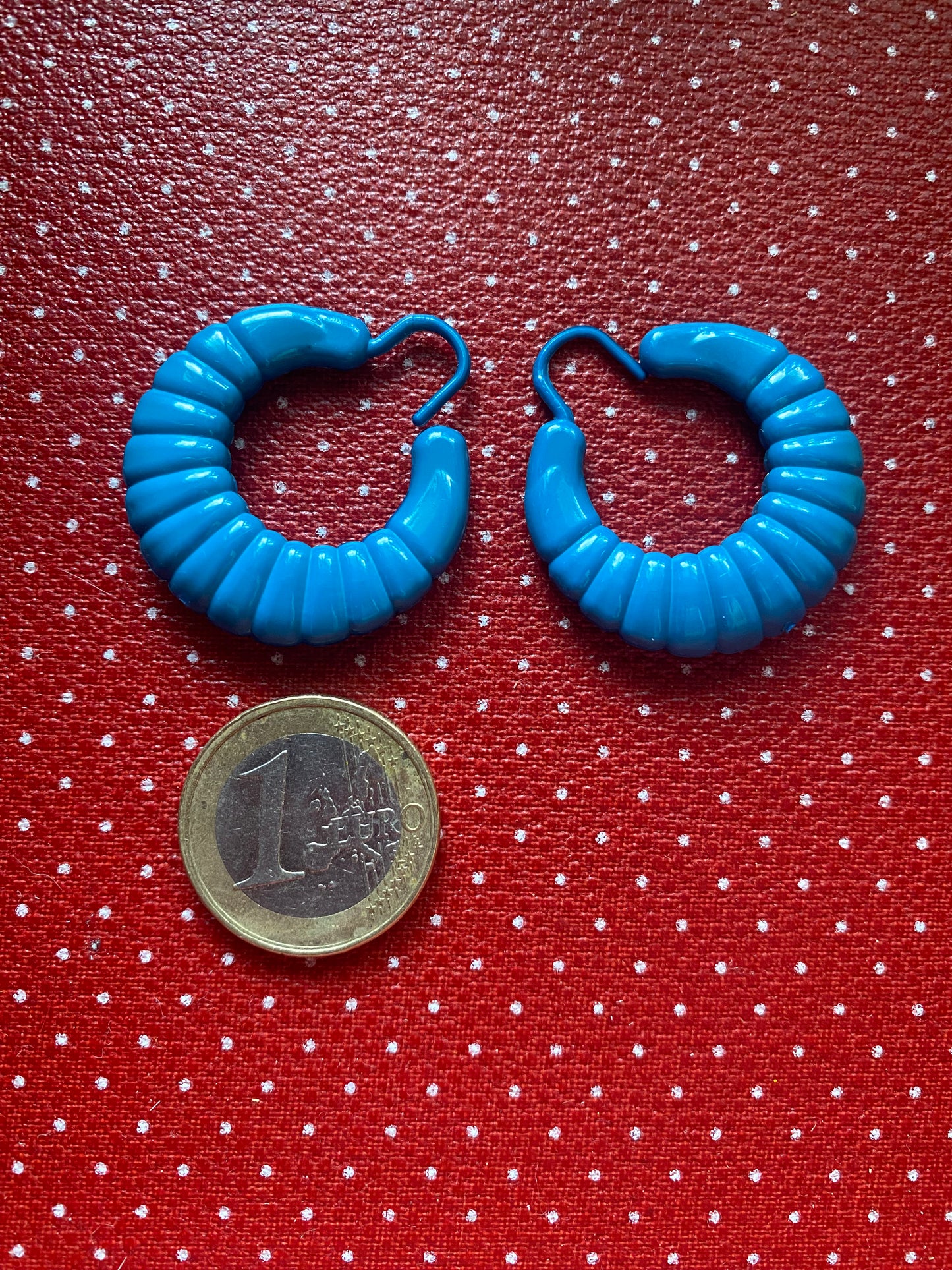 Blue authentic 80s hoop earrings on a red polka dot background with a coin for scale.