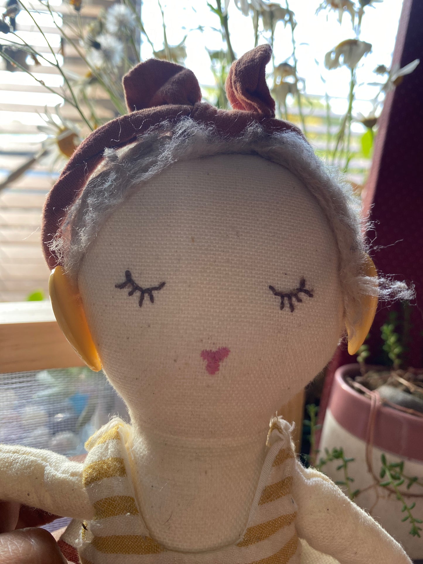 Close-up of a plush toy modelling the earrings with a striped outfit and headband, blurred background