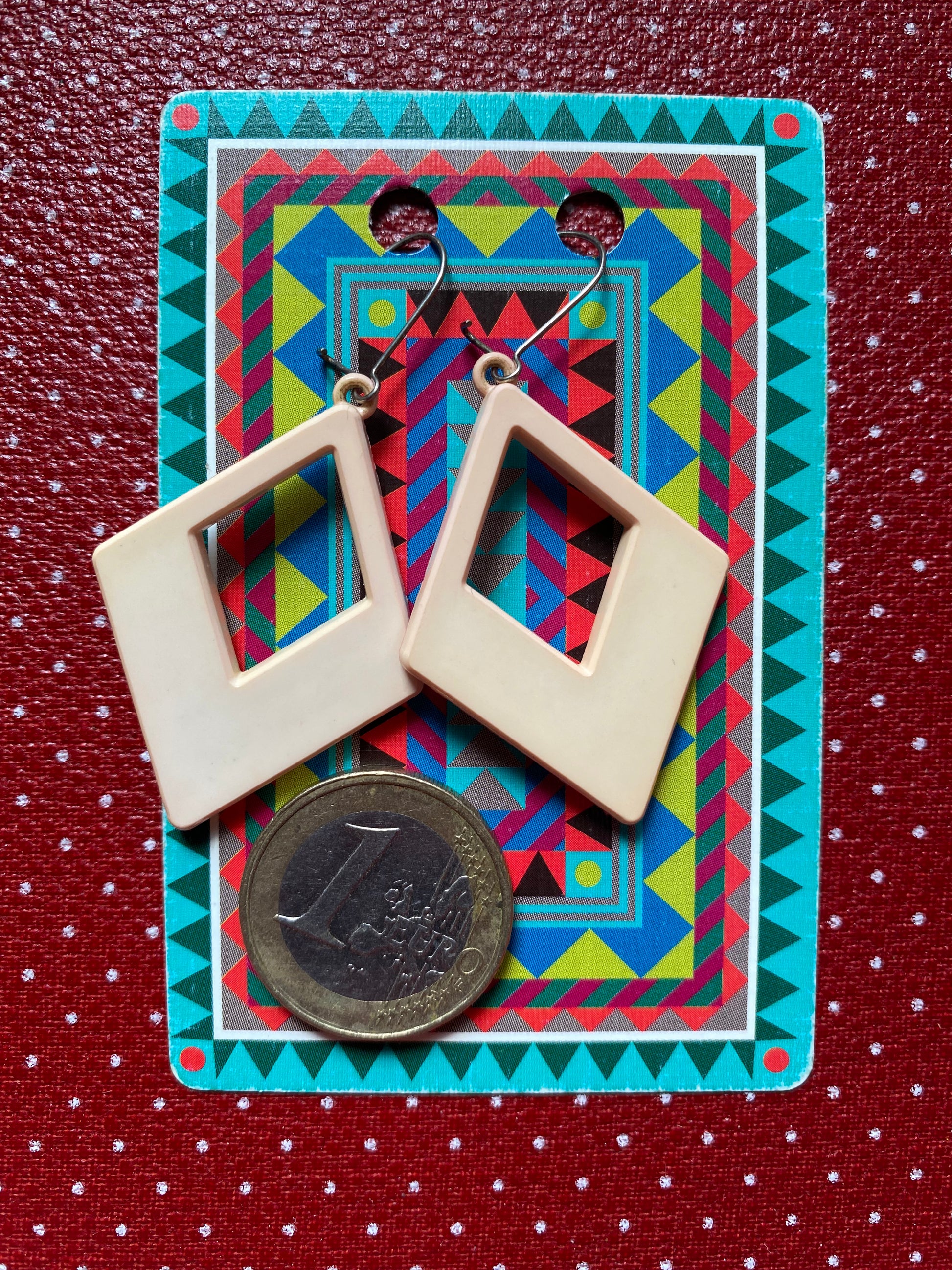 Authentic 80s Beige diamond shaped earrings on a colorful card with a coin for size reference, against a red retro polka dot background.