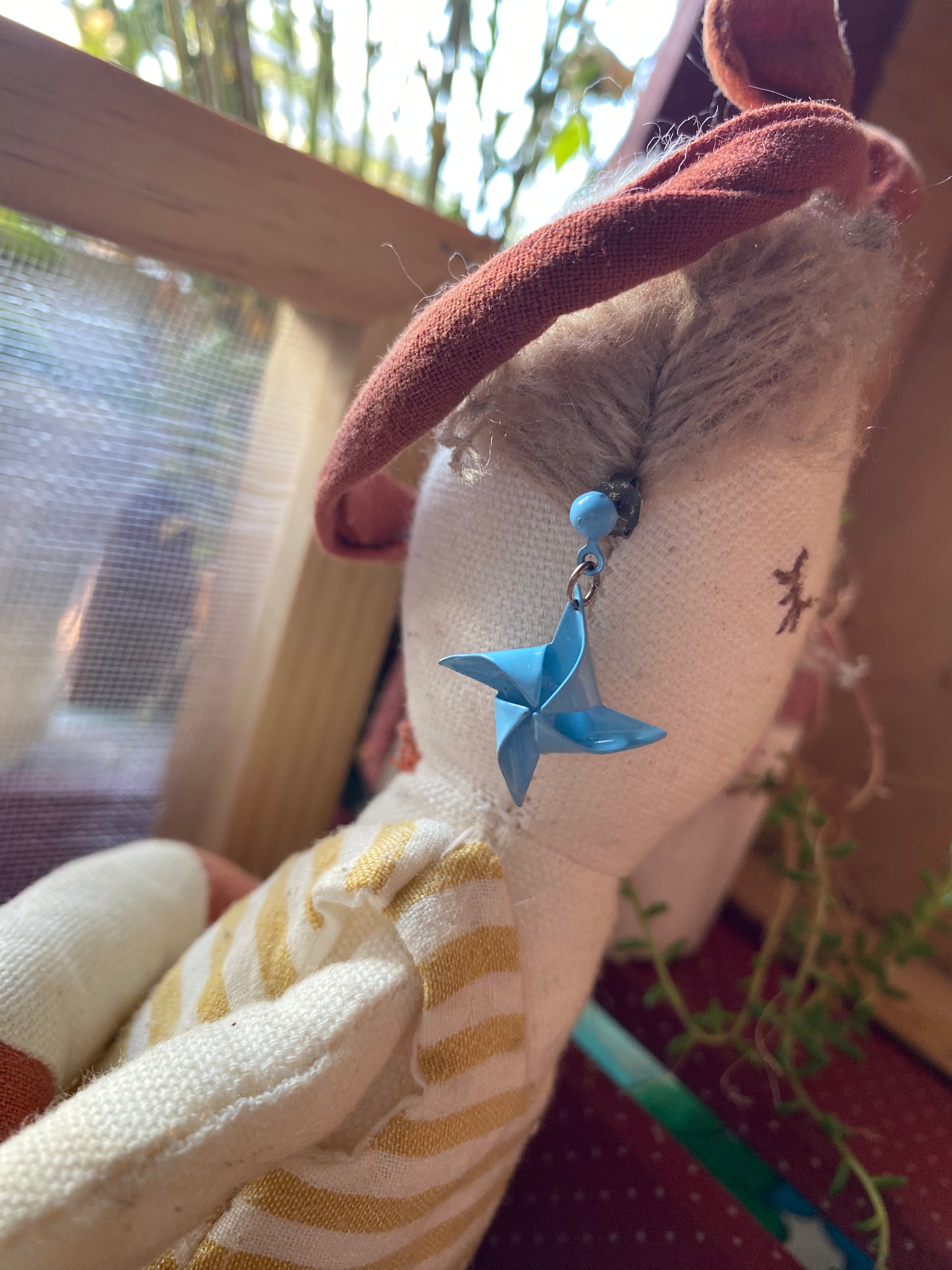 Close-up of a plush toy model with a pair of 80s blue star charm earrings , blurred background