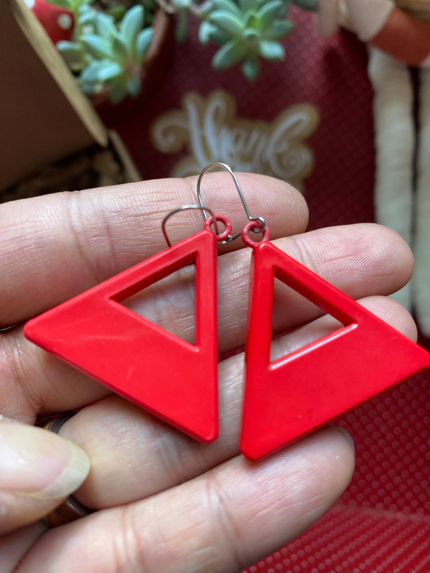 Red 80s triangle-shaped earrings held in a hand with a blurred background