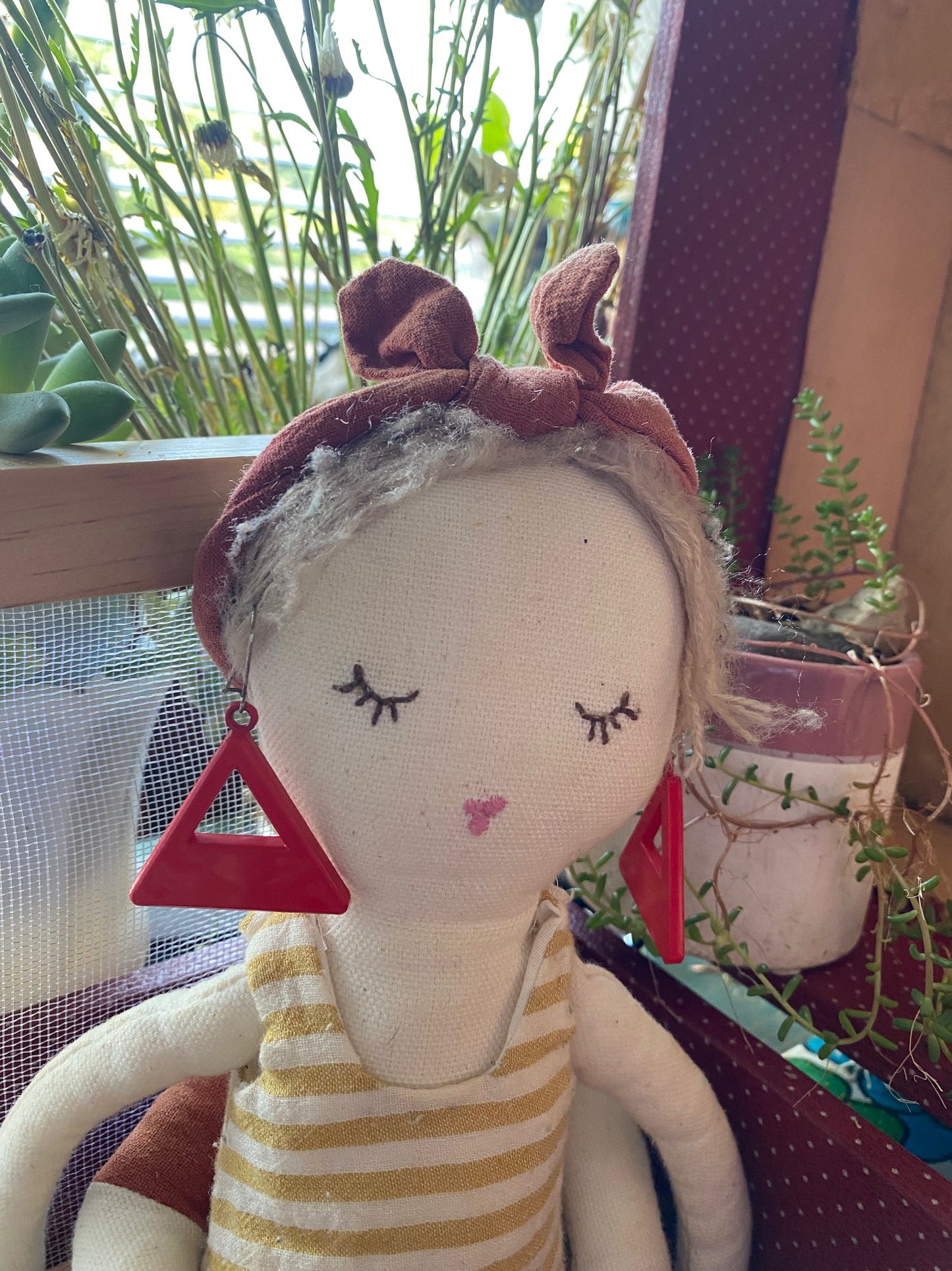 A model with a striped shirt wearing a pair of red authentic 80s earrings in a natural setting with plants.