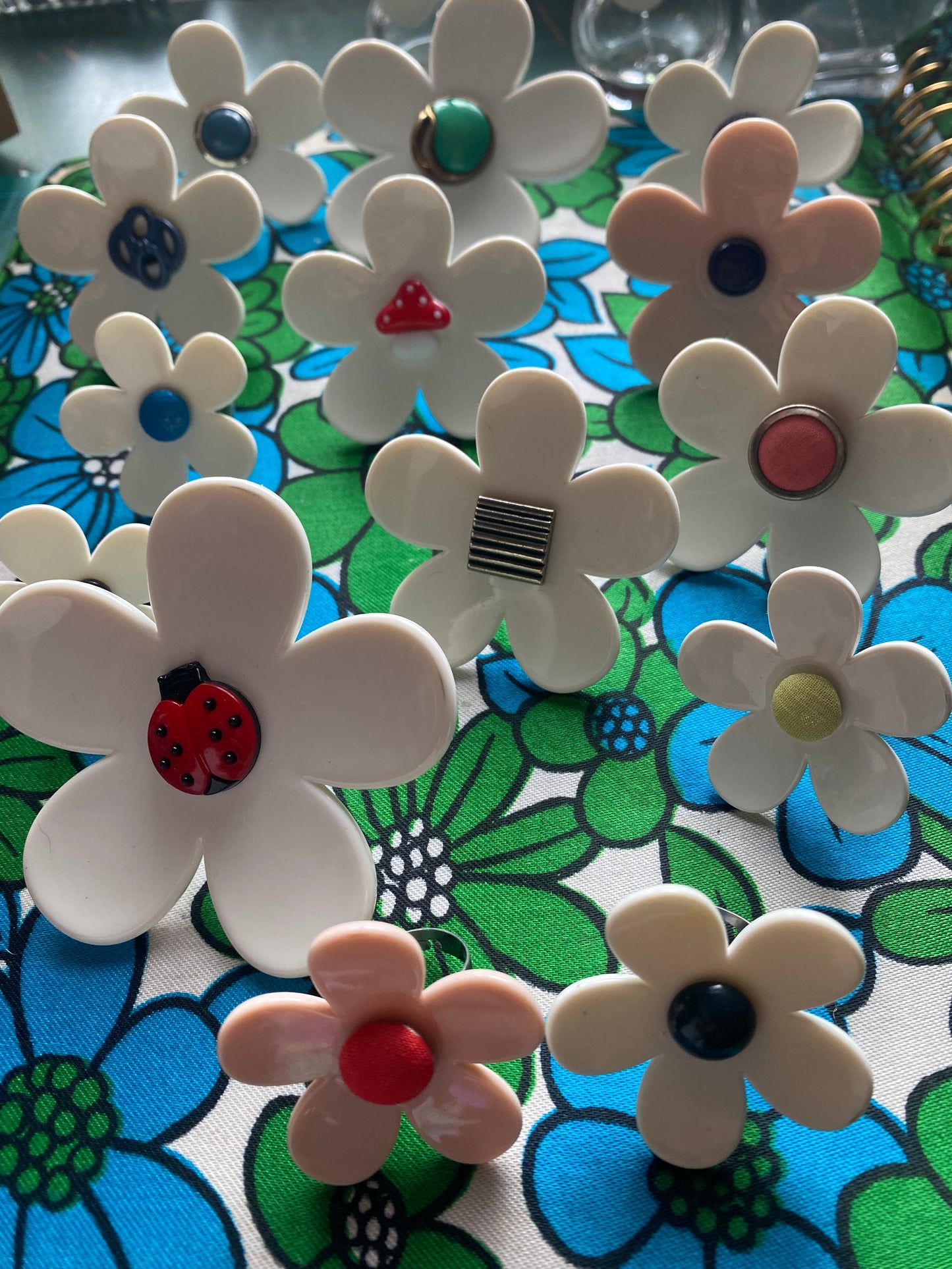 Handmade white daisy flowers rings with colorful centers on a retro floral-patterned surface