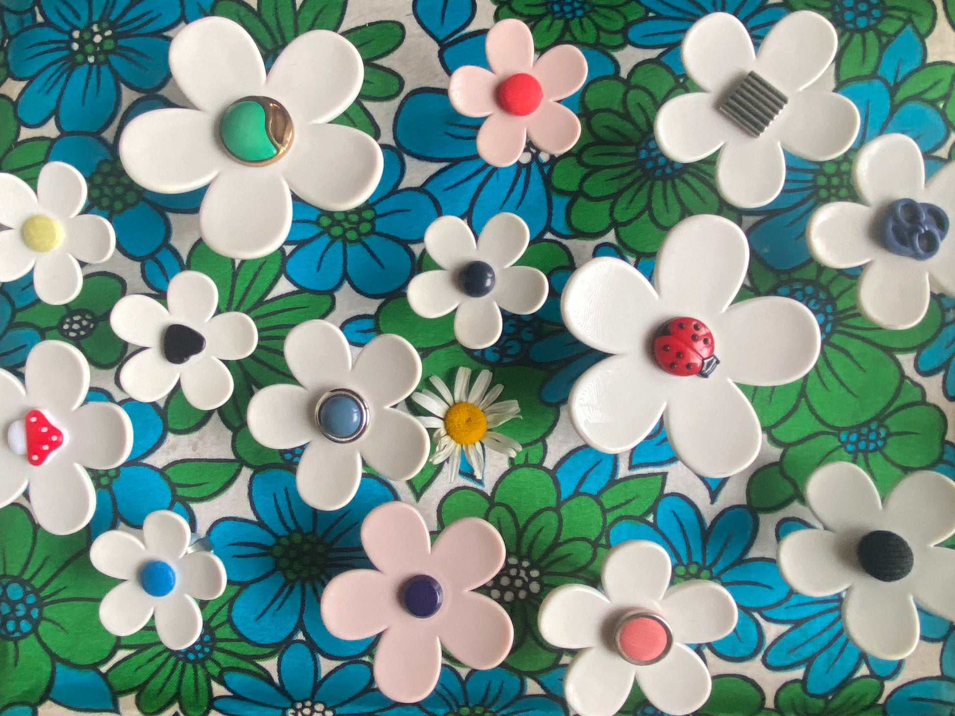 A collection of Colorful up-cycled handmade plastic daisy flowers rings with ladybugs and other styles of bottom on it and varies sizes a floral patterned background