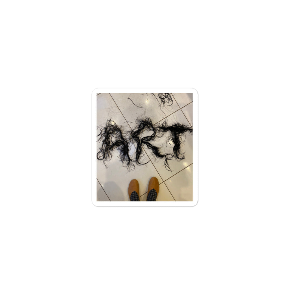 Photography of freshly cut hair spelling ART on floor with feet in view 
