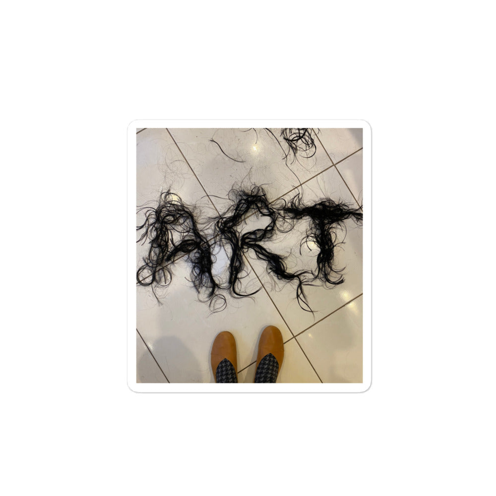 Photography of freshly cut hair spelling ART on floor with feet in view