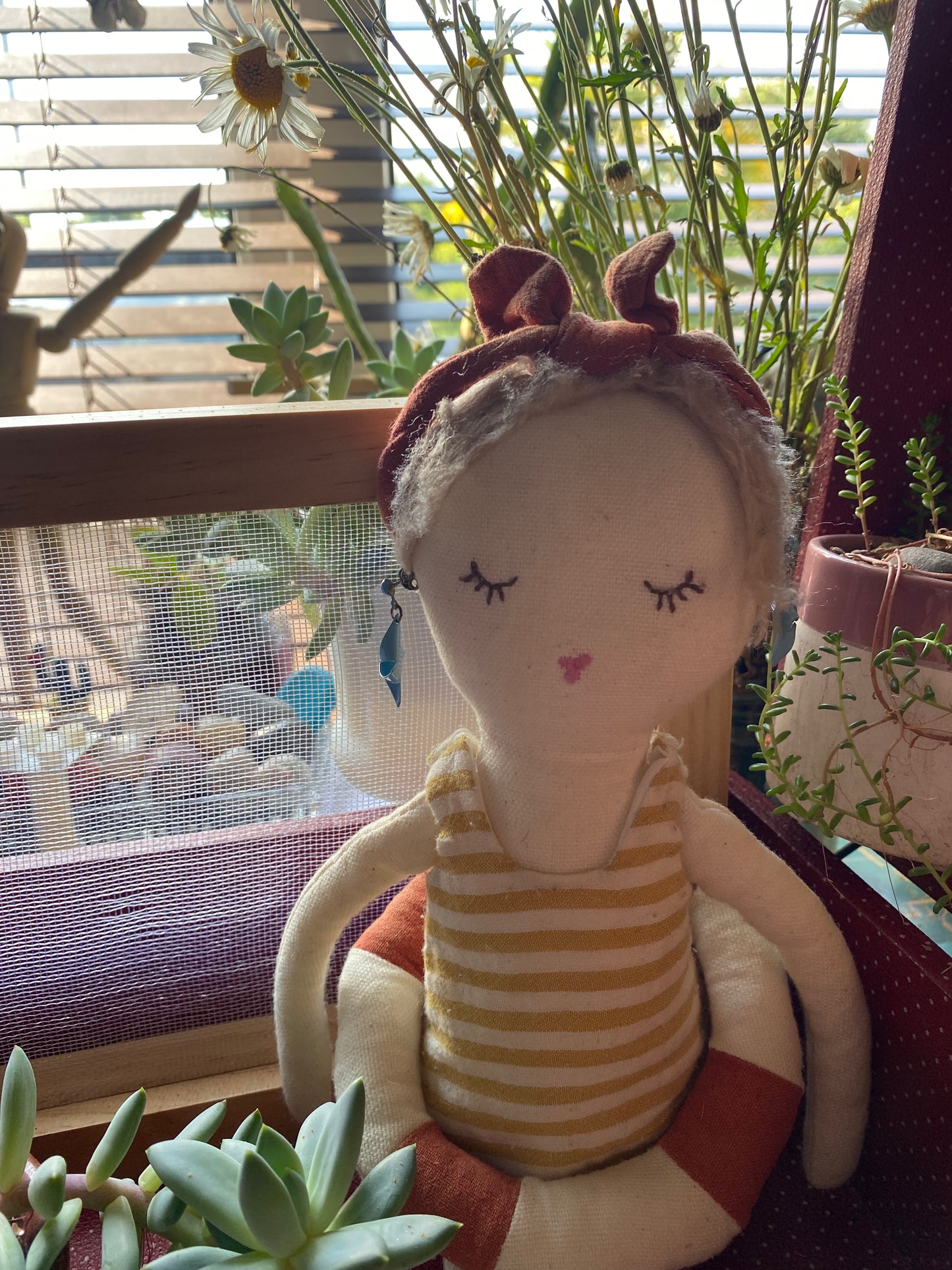 Modelling the blue earrings wearing a striped dress with plants in the background
