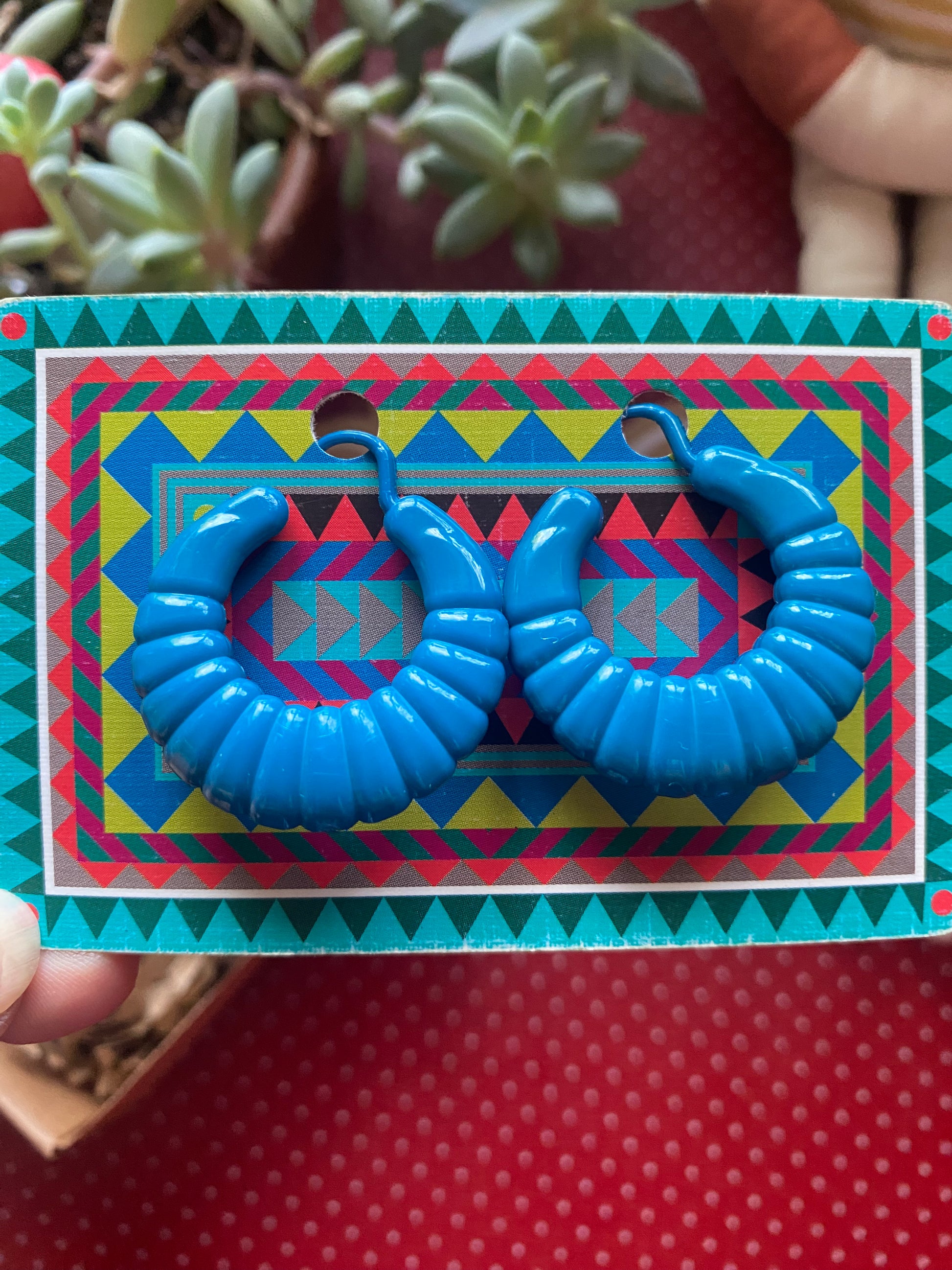 Blue 80s earrings on a colorful geometric card with plants in the background