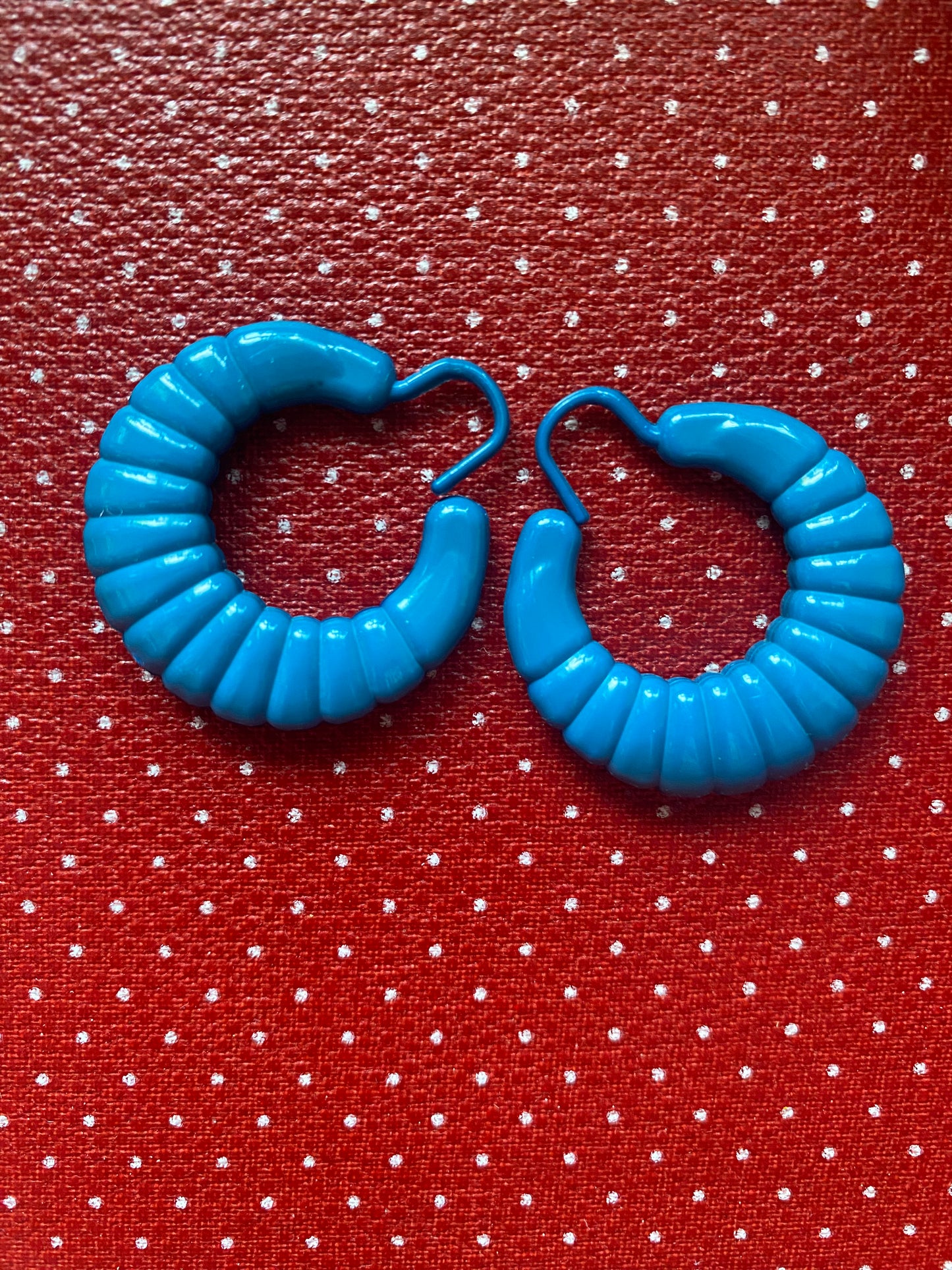 Blue hoop 80s earrings on a red fabric background with white polka dots