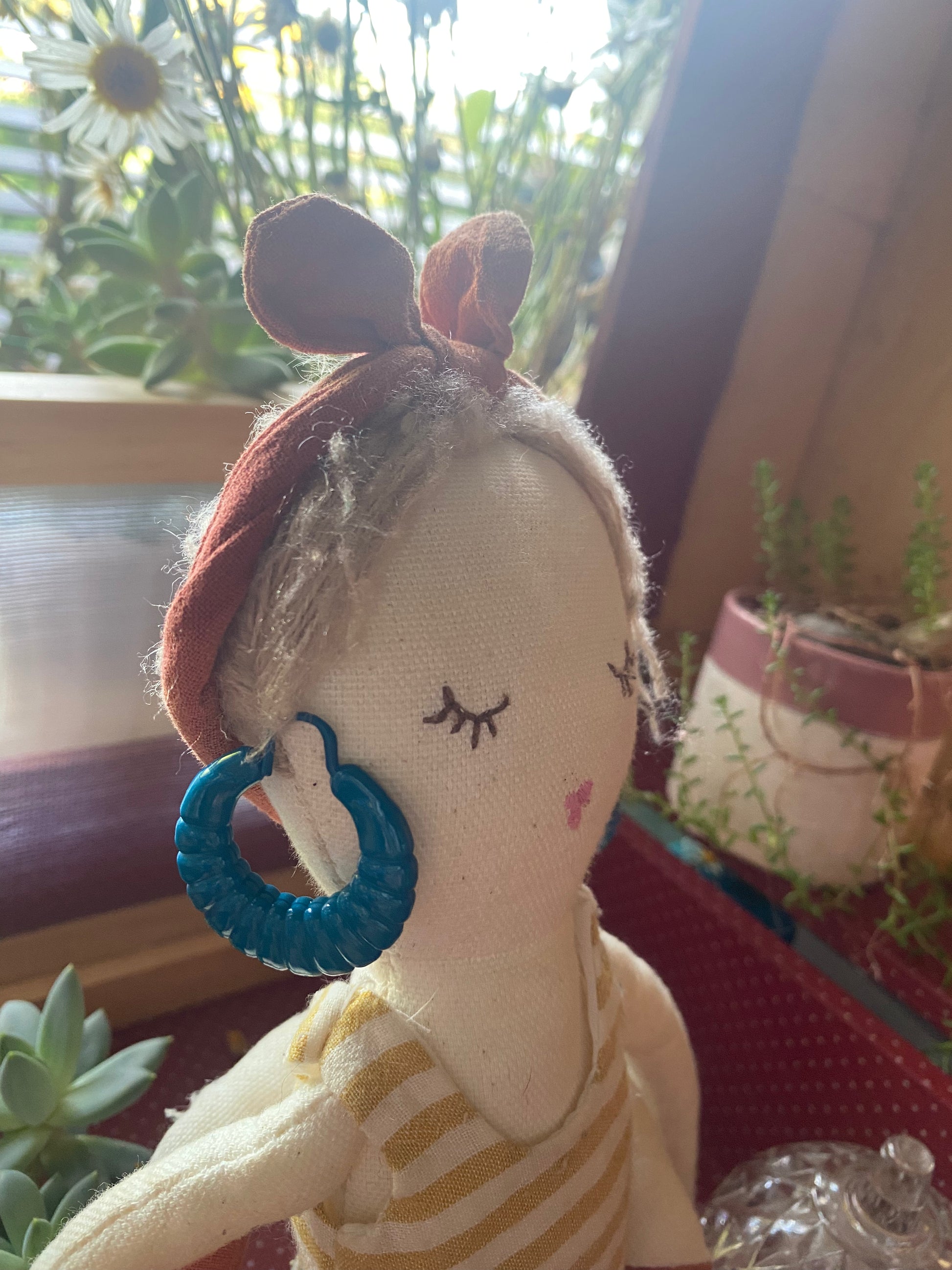 Textile doll with a blue 80s earring in a natural setting with plants