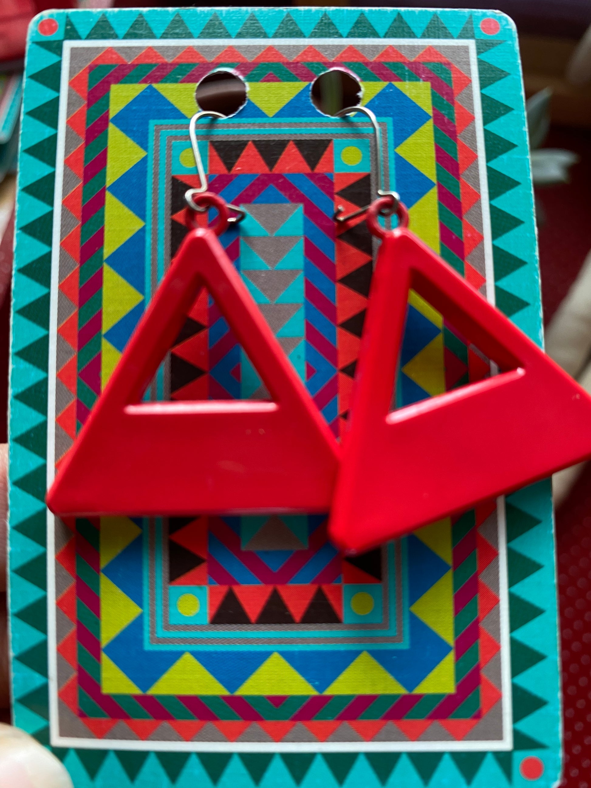 Red authentic 80s triangle-shaped earrings on a colorful geometric-patterned card