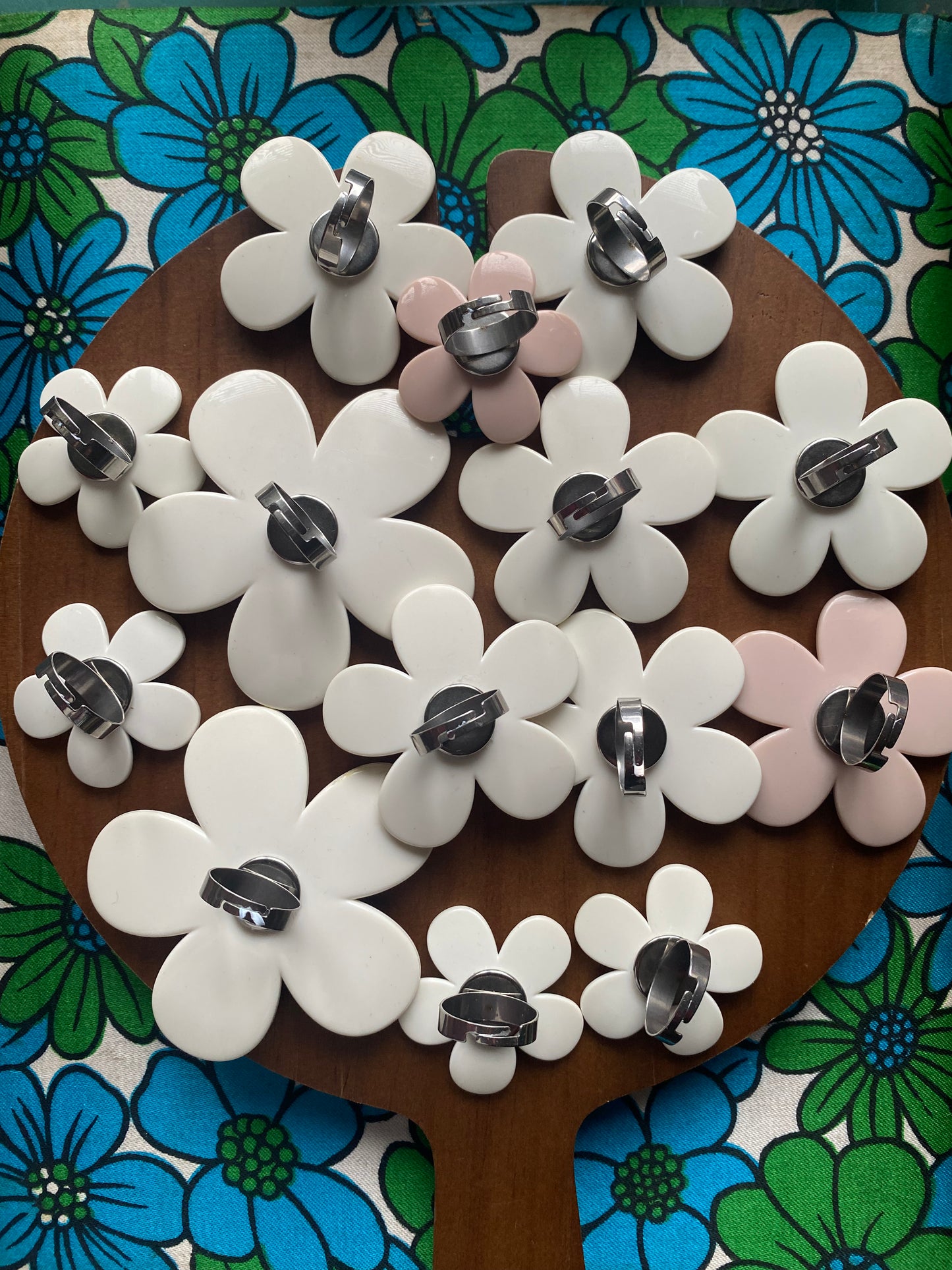 show casing the back of the daisy Flower-shaped rings on a wooden board with a floral-patterned background