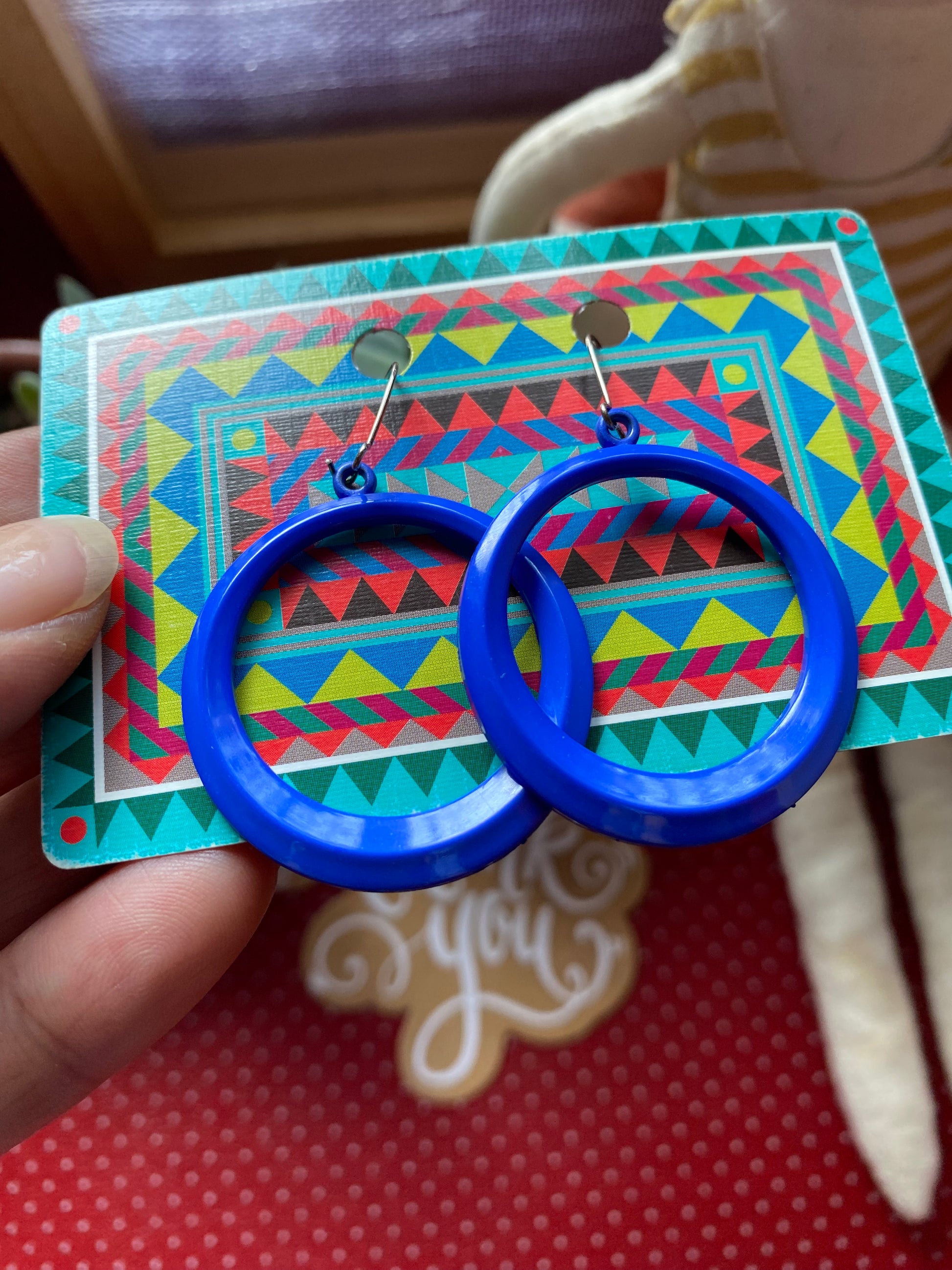 Blue 80s hoop earrings on a colorful card held by a hand.