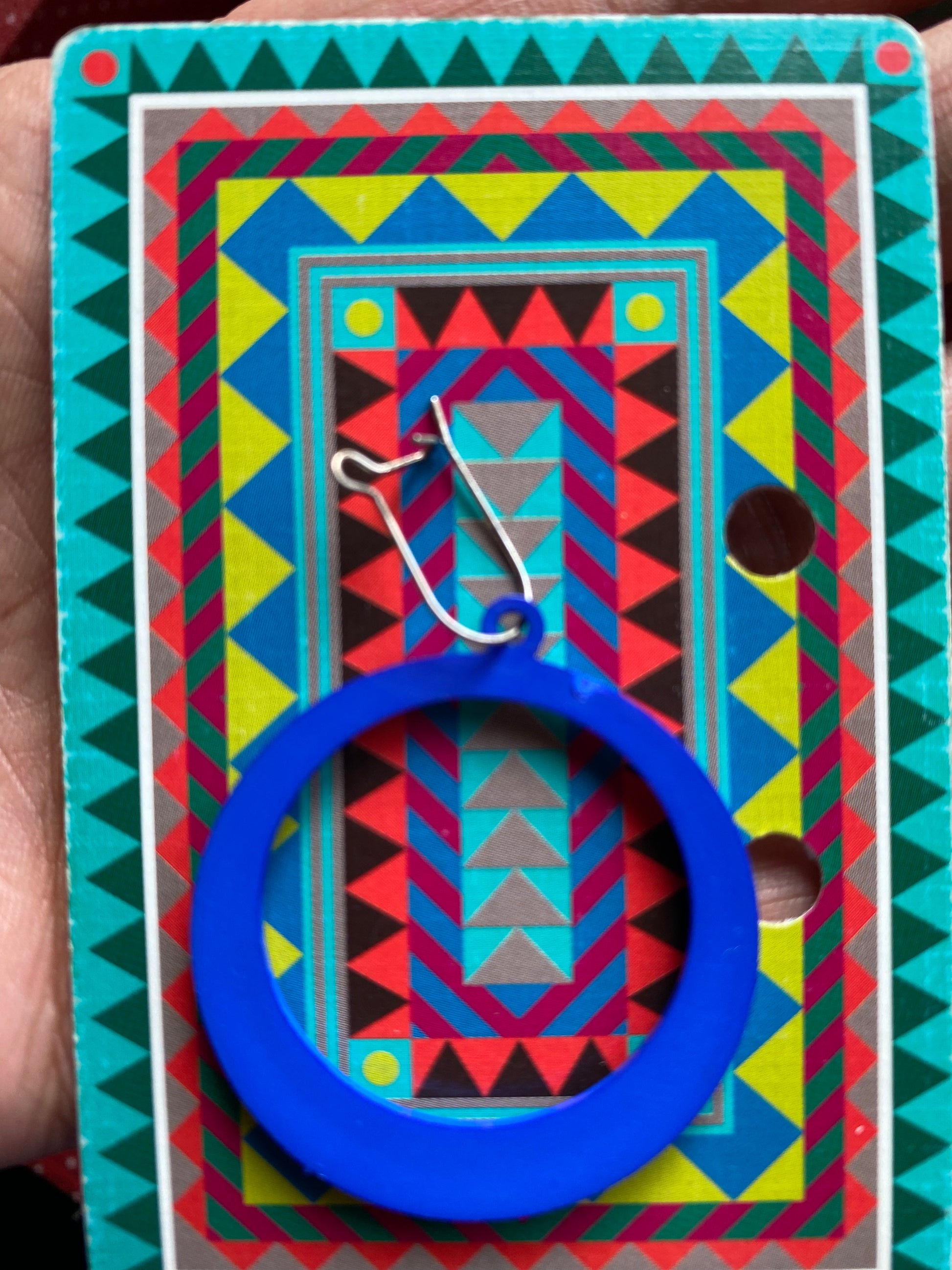 Colorful geometric-patterned card with a blue 80s earring and silver hook on a textured surface.
