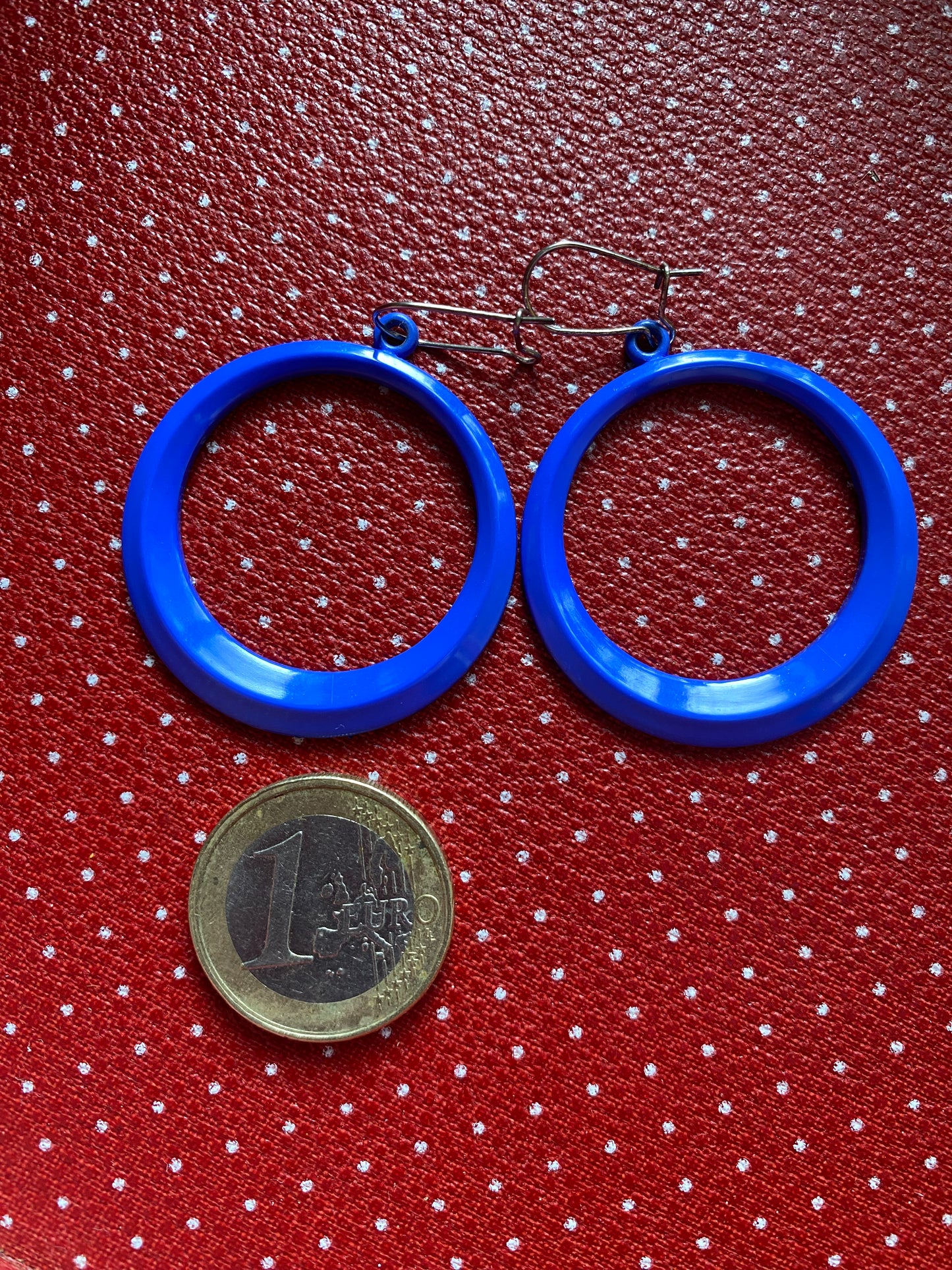 Blue 80s hoop earrings on a red polka dot background with a coin for scale.