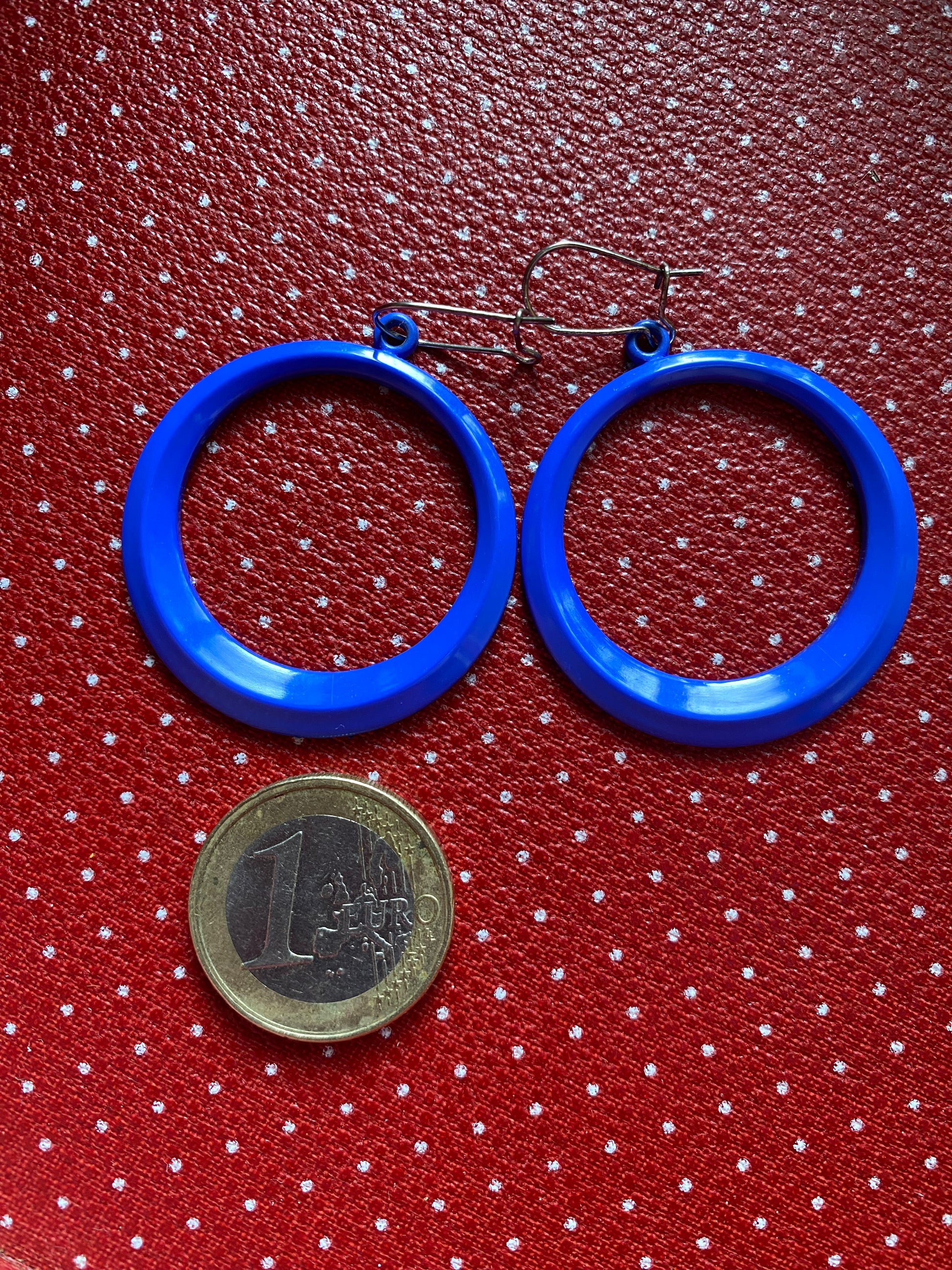 Blue 80s hoop earrings on a red polka dot background with a coin for scale.