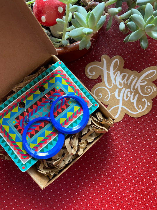 Blue circular authentic 80s earrings on a colorful card with a 'thank you' note and plants in the background.