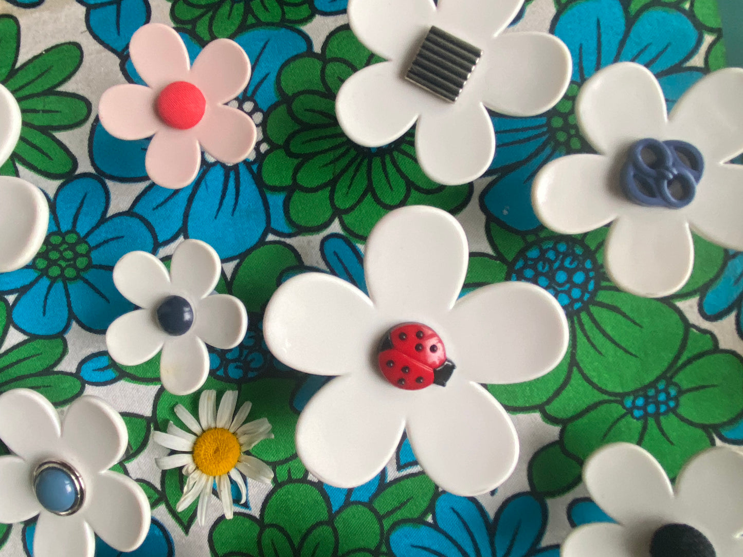 A collection of handmade upcycled daisy rings. Colorful floral pattern with white flowers featuring ladybugs on a textured background