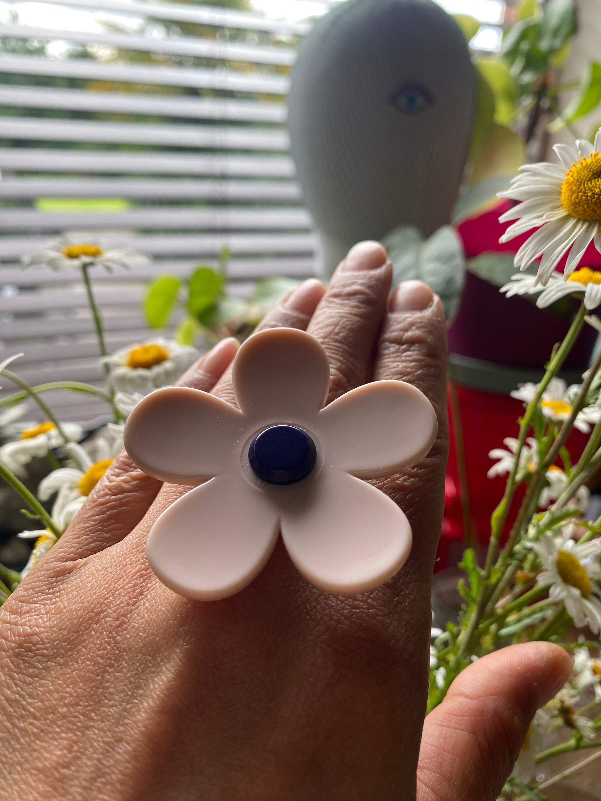 Handmade white daisy flower-shaped ring with a blue center held by a hand against a happy background