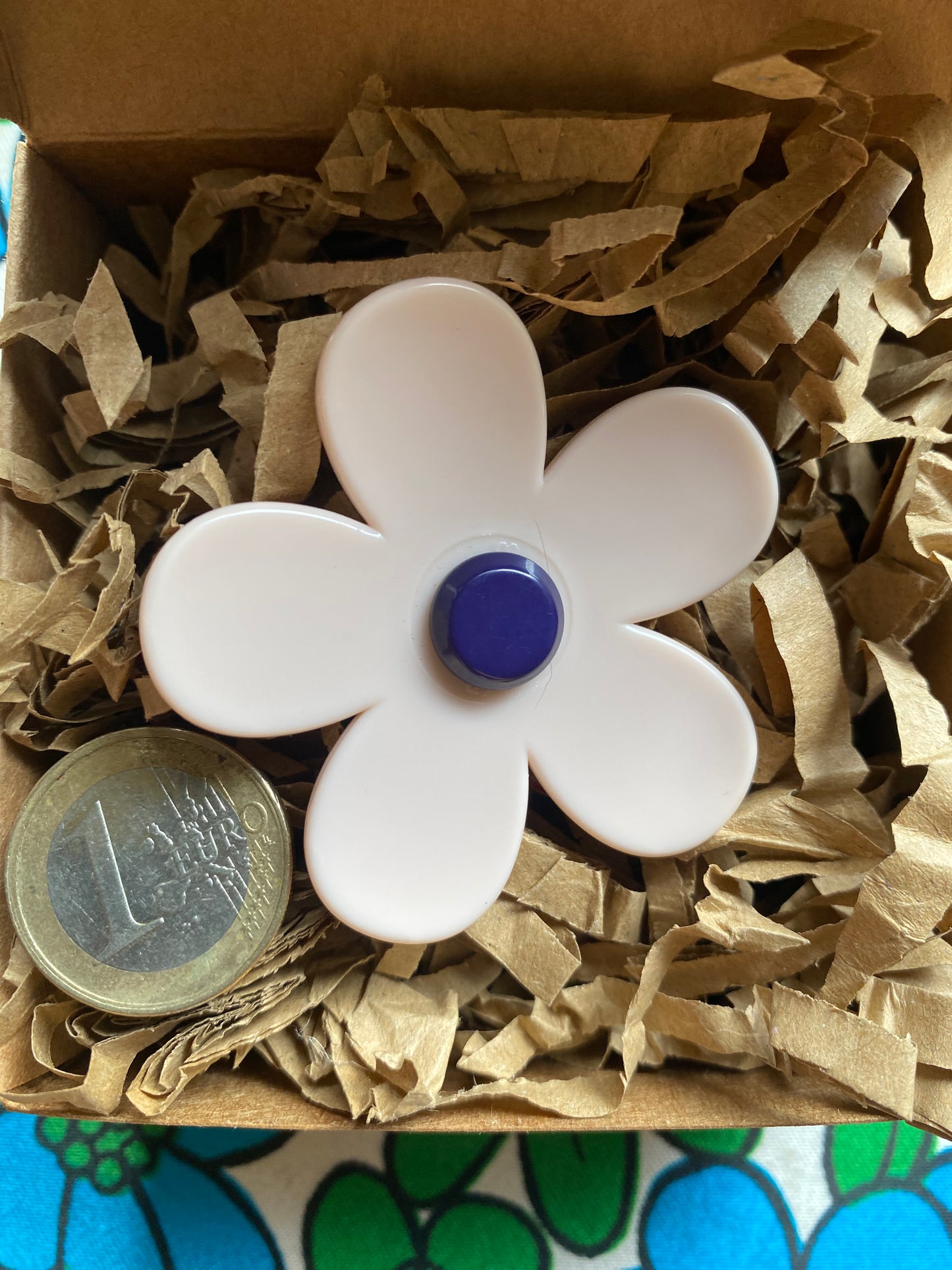 White handmade daisy flower-shaped ring with a blue center on brown paper inside a gift box.