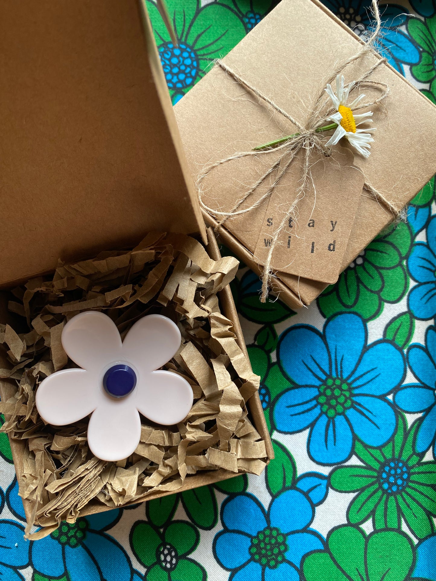 Small gift box with decorative flower and text 'stay wild' on a floral-patterned surface.