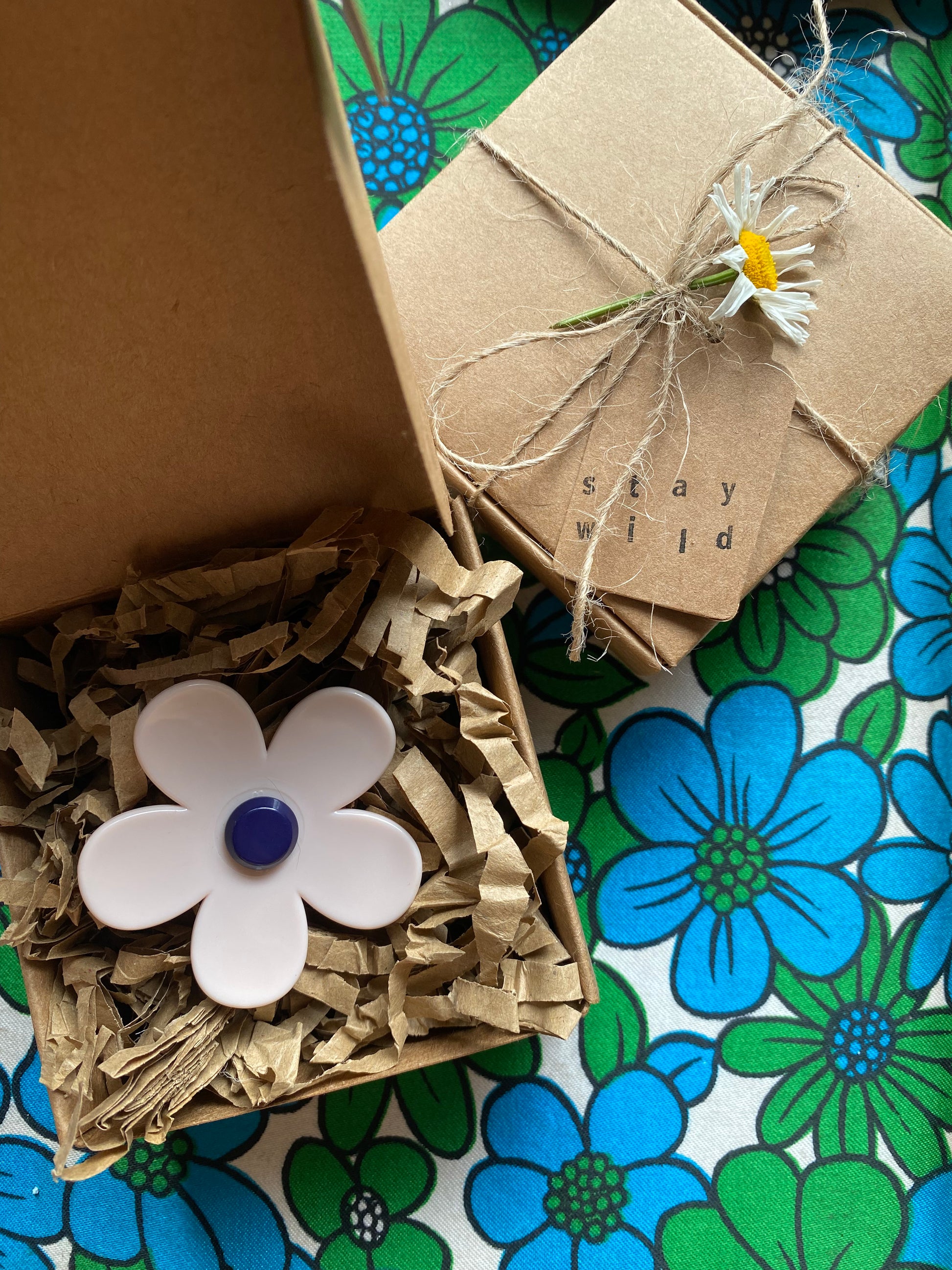 Small gift box with decorative flower and text 'stay wild' on a floral-patterned surface.