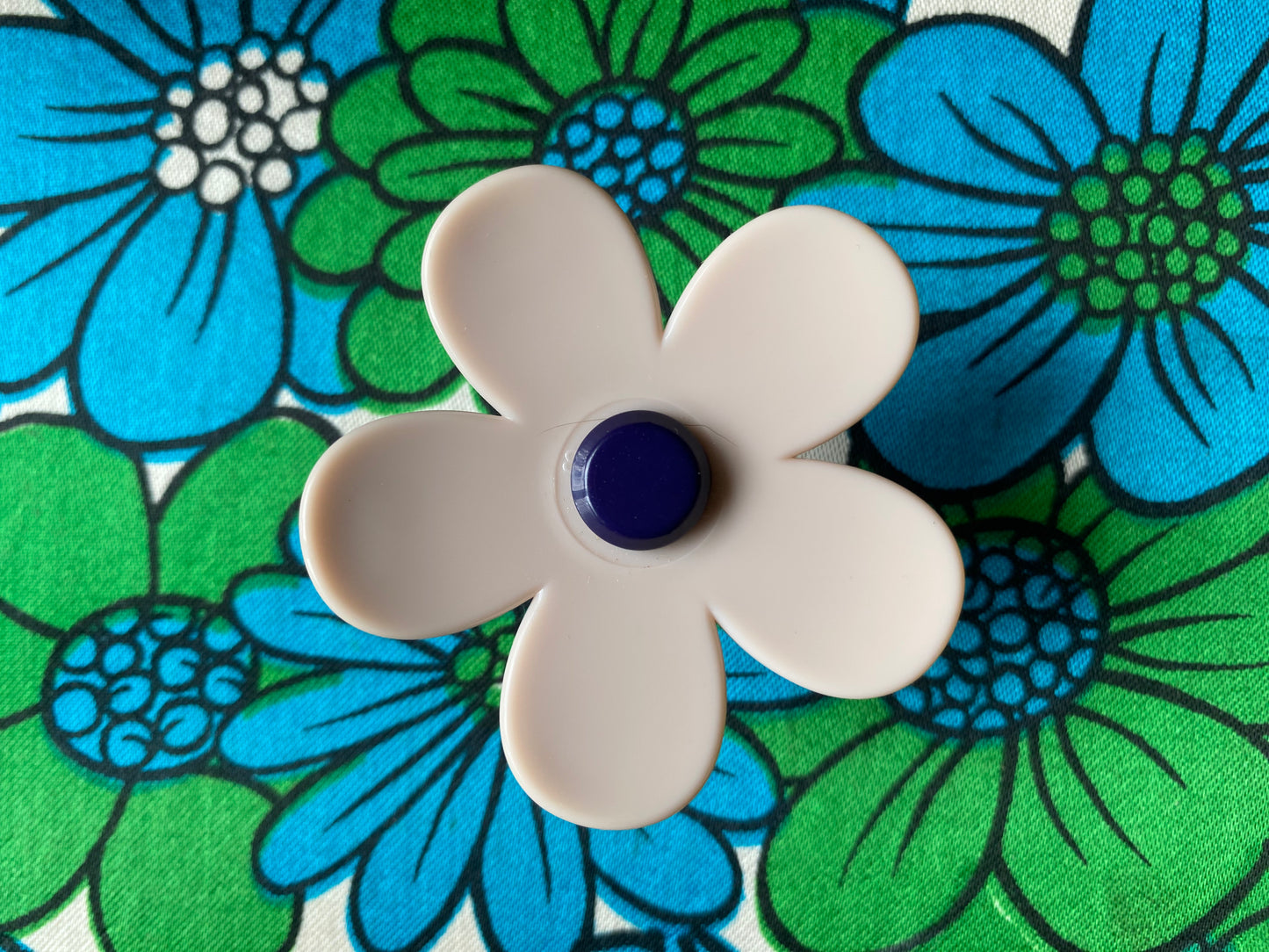 Handmade white daisy flower-shaped ring with a blue center on a floral background