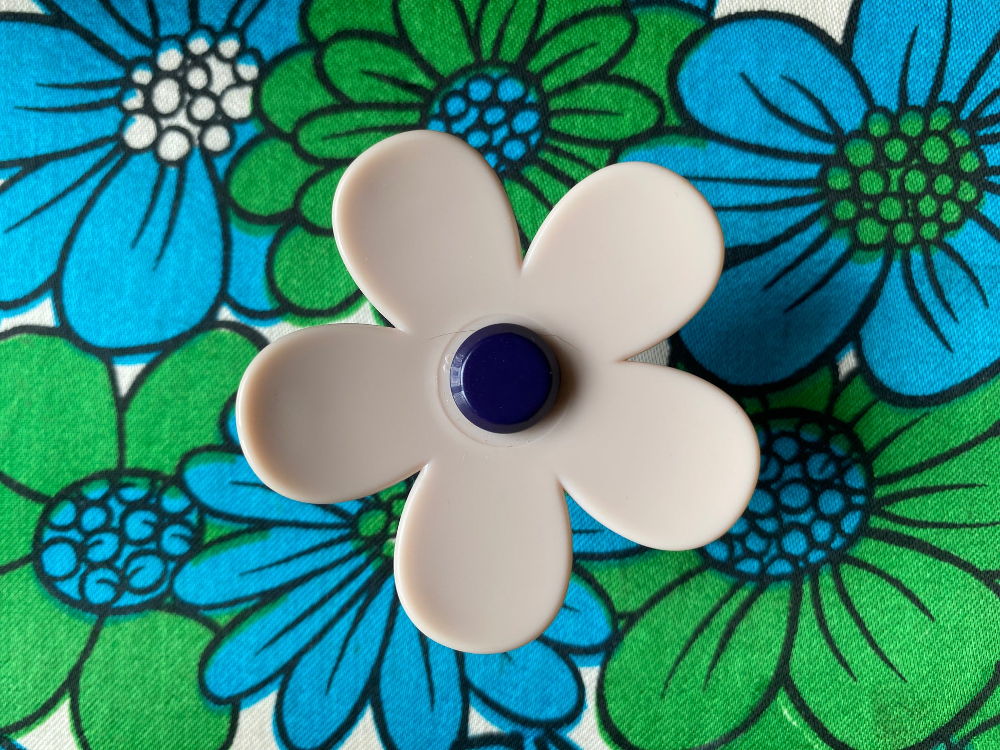 Handmade white daisy flower-shaped ring with a blue center on a floral background