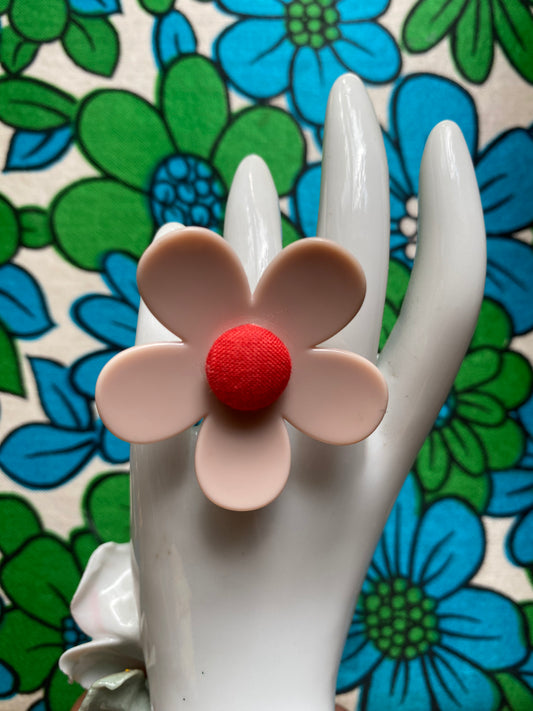 Handmade daisy Flower-shaped ring with a red center on a white hand against a floral background