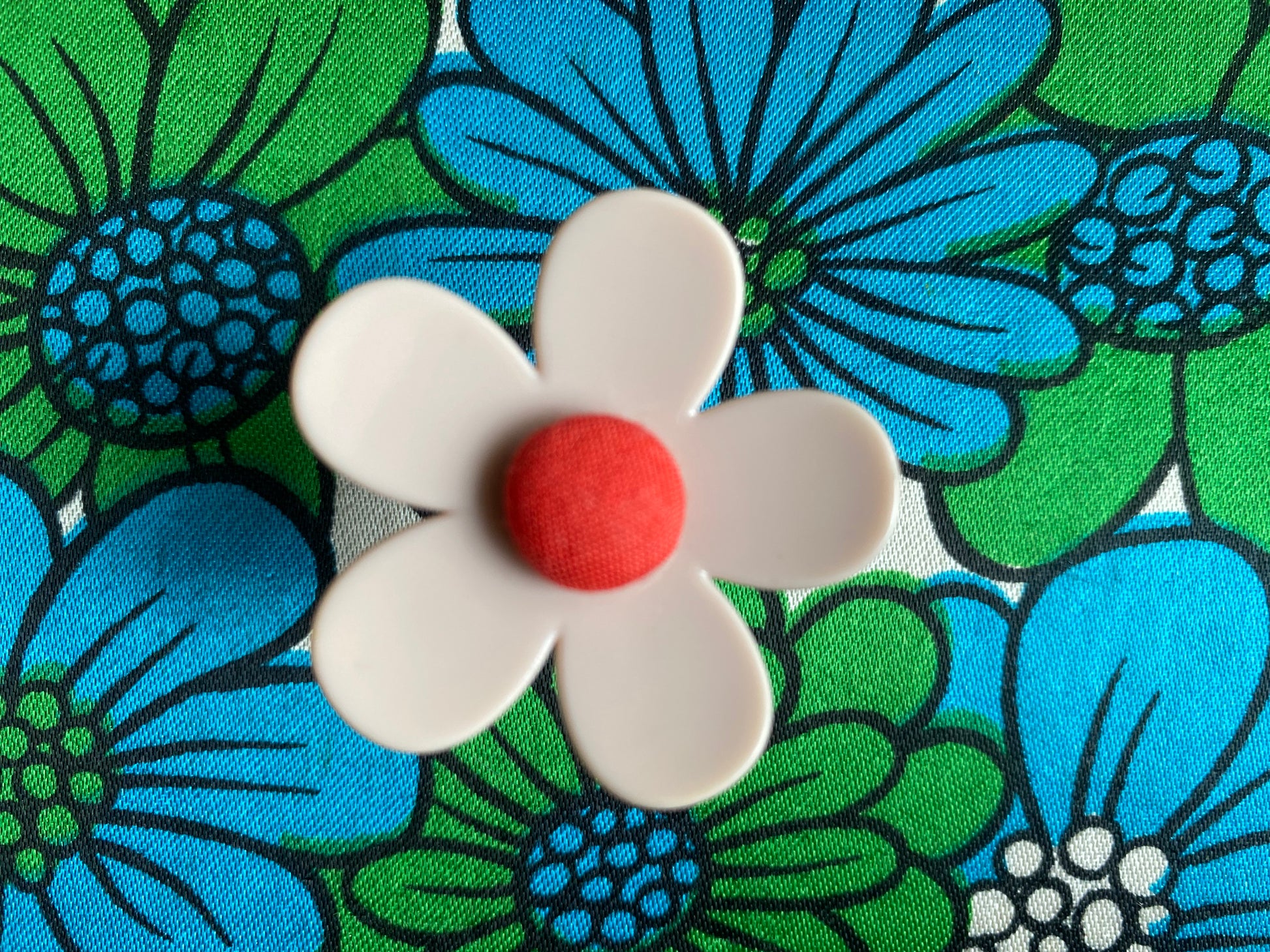 Handmade pink daisy flower-shaped ring with a red center on a colorful floral background
