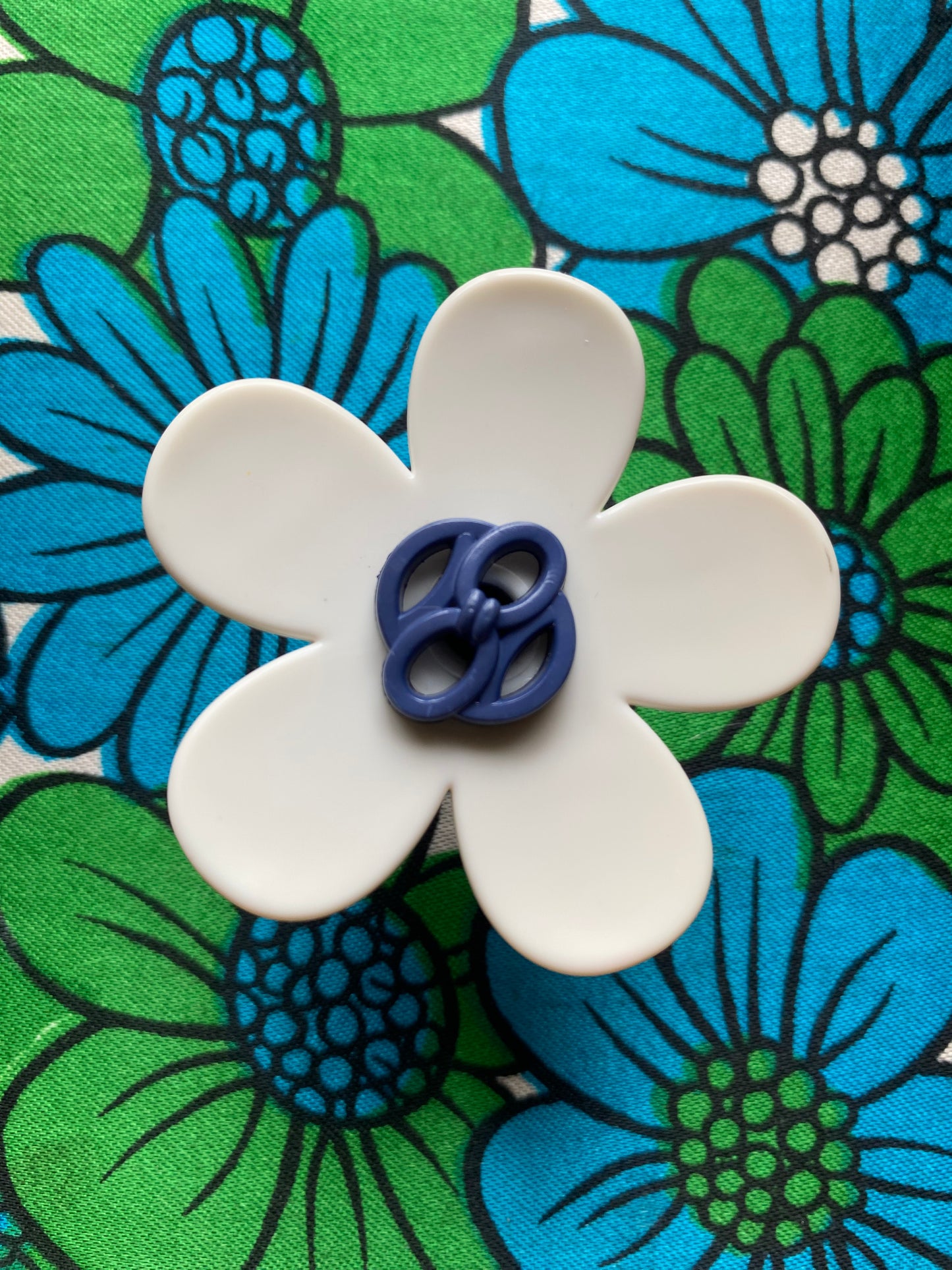 White handmade daisy flower-shaped ring with a blue center on a floral background