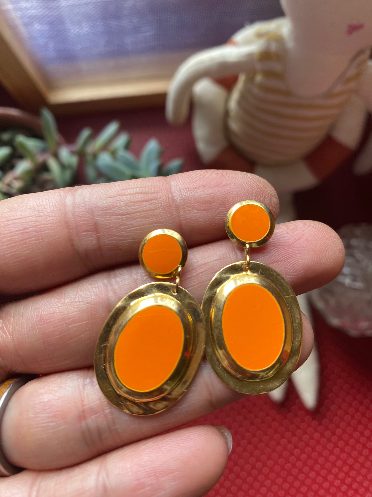 Orange 80s earrings with gold accents held between fingers against a blurred background