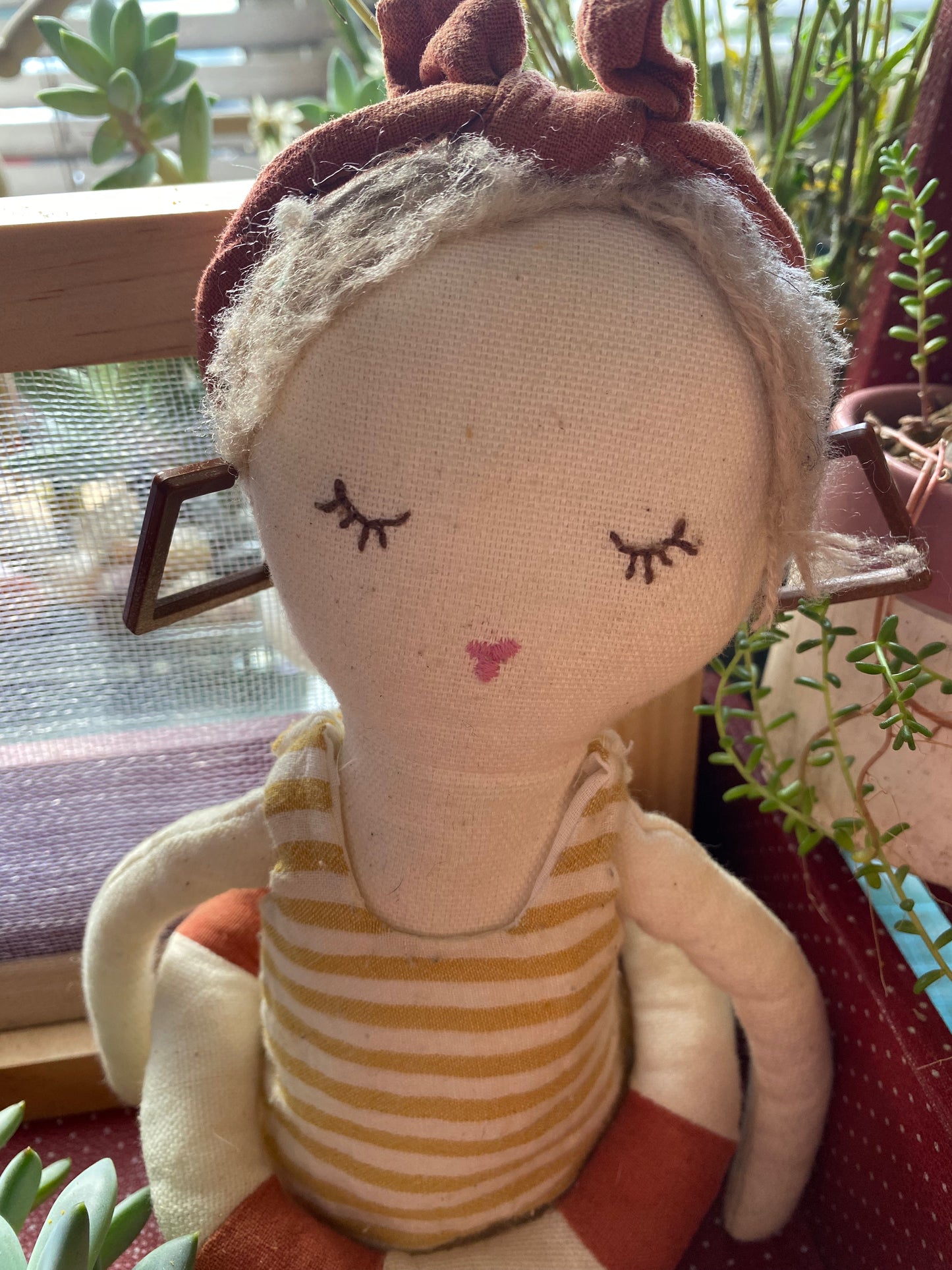 Textile doll modelling the earrings with a striped dress and headband in a natural setting