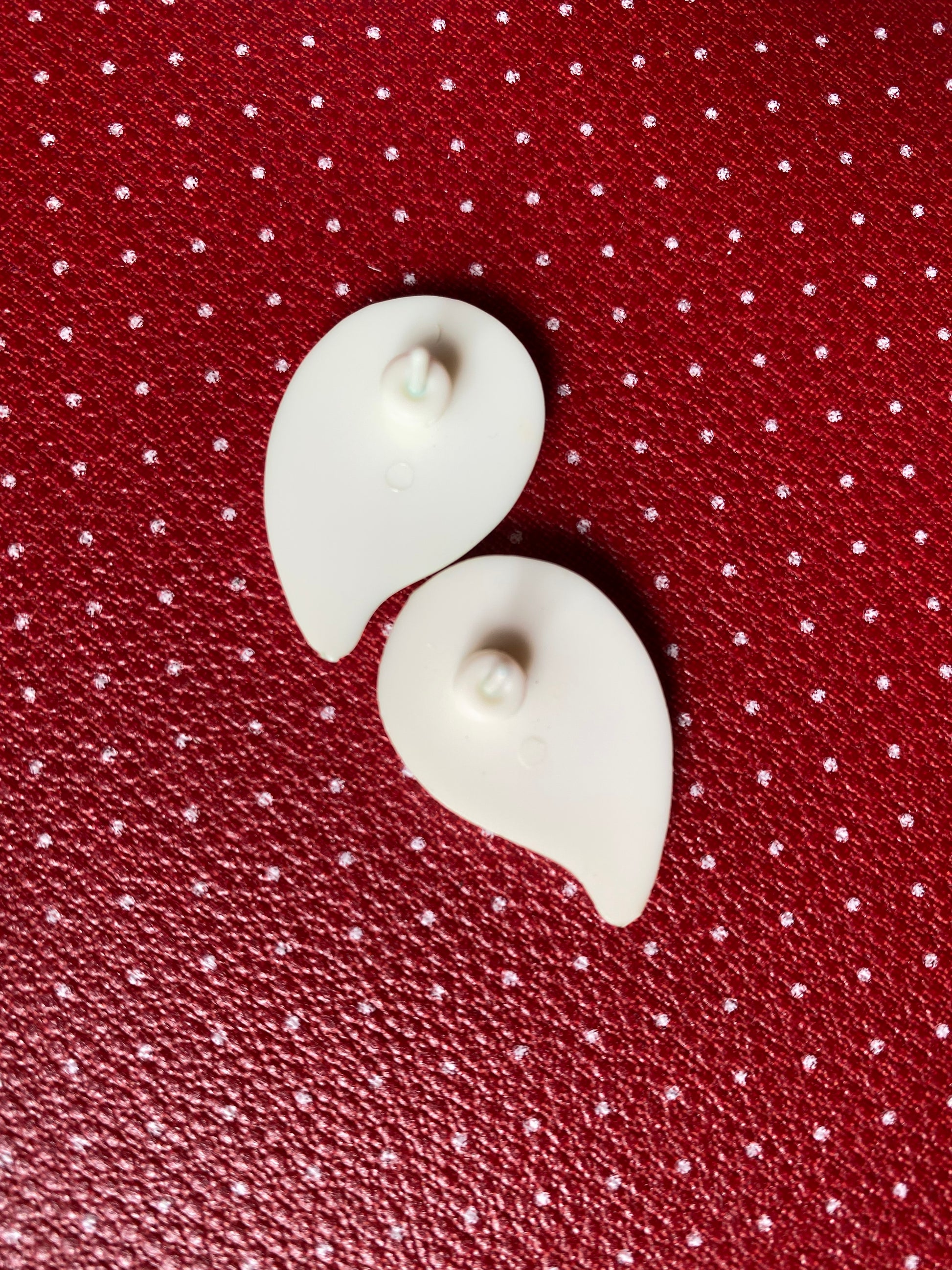 Showing the back of the white earrings on a red polka dot background