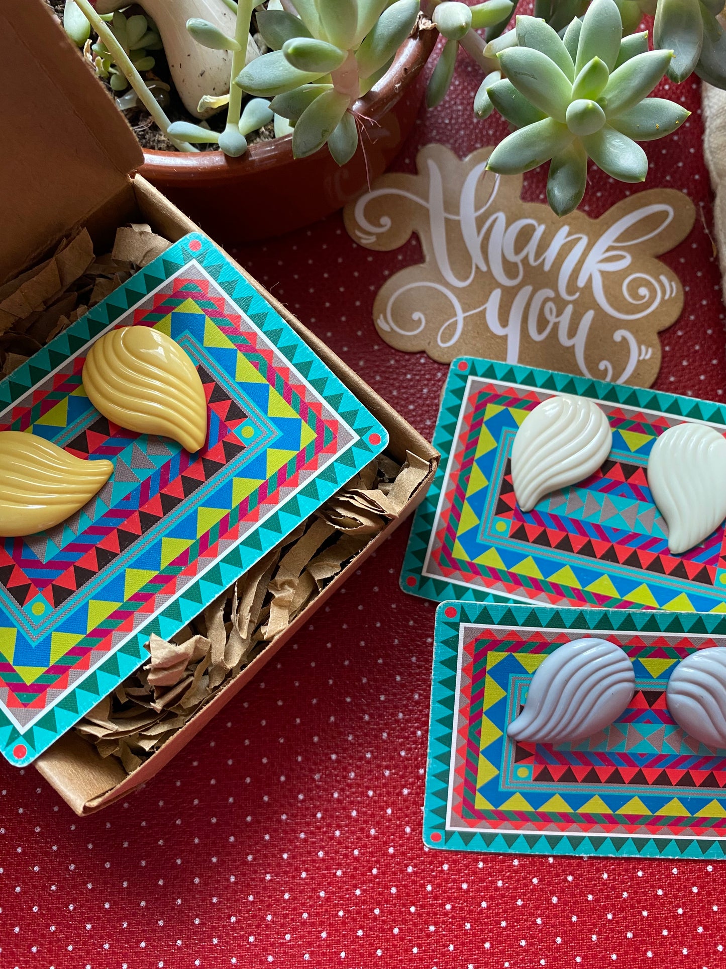 Colorful earrings with shell designs on a red retro surface with 'Thank You' card.