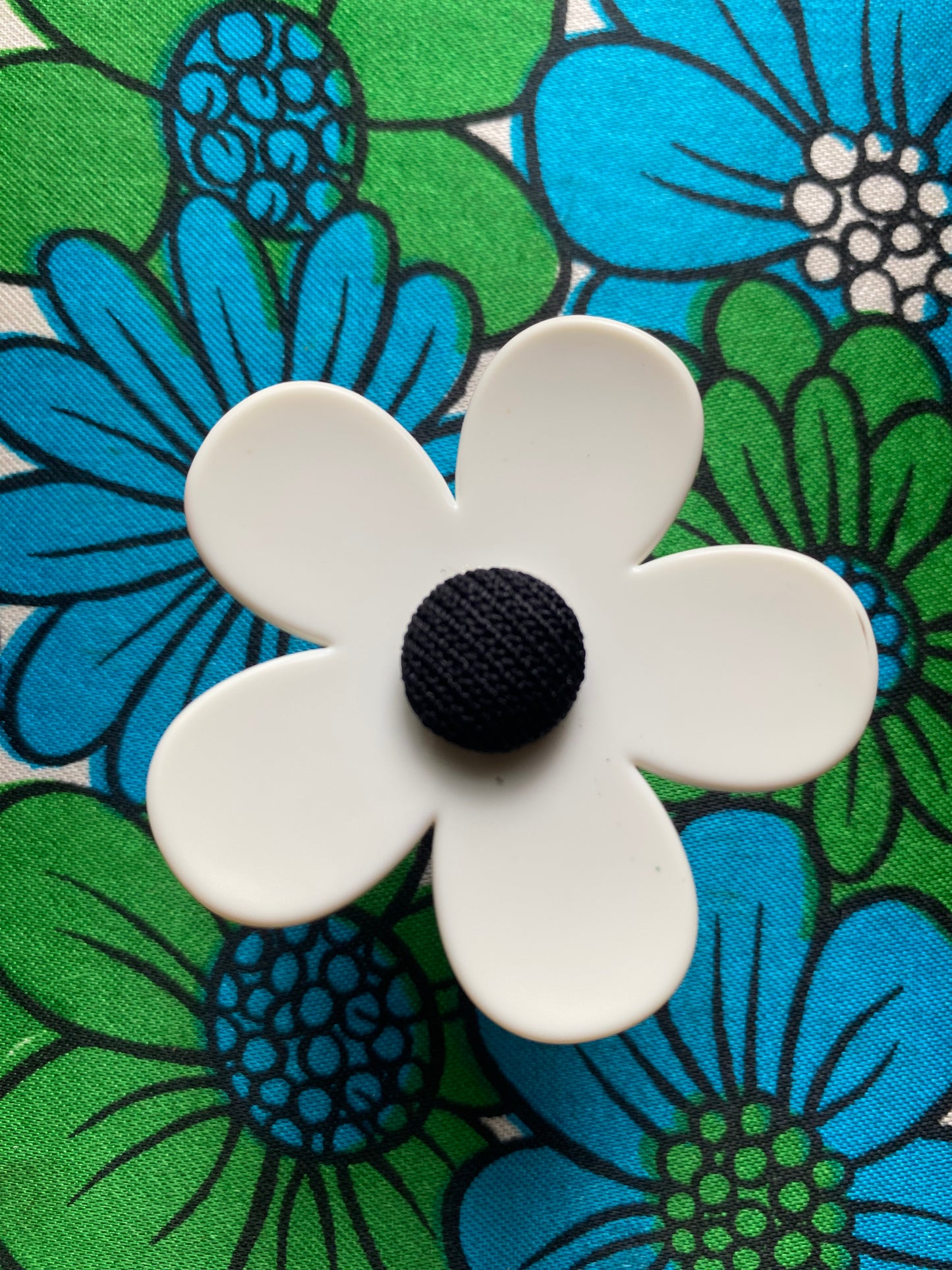 Handmade White daisy flower-ring with a black center on a floral fabric background