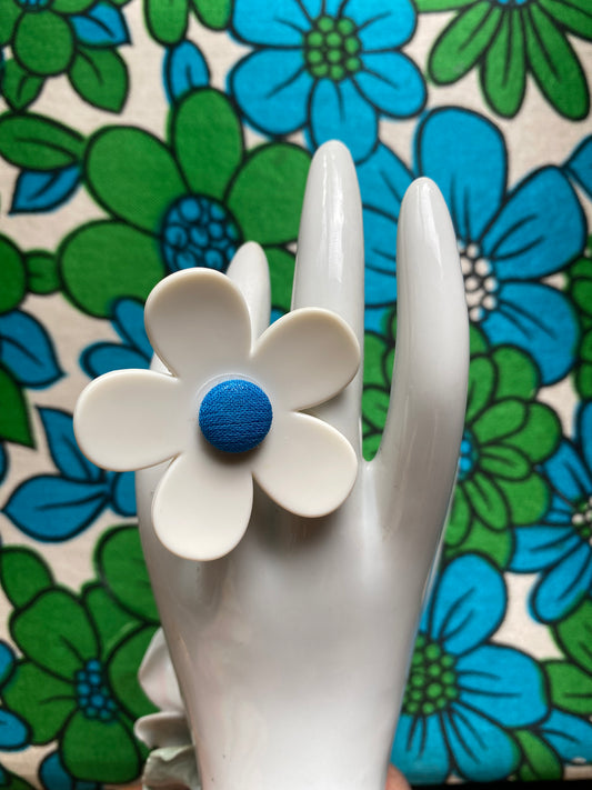 Handmade upcycled White daisy  flower-shaped ring with a blue center on a white hand model against a floral background
