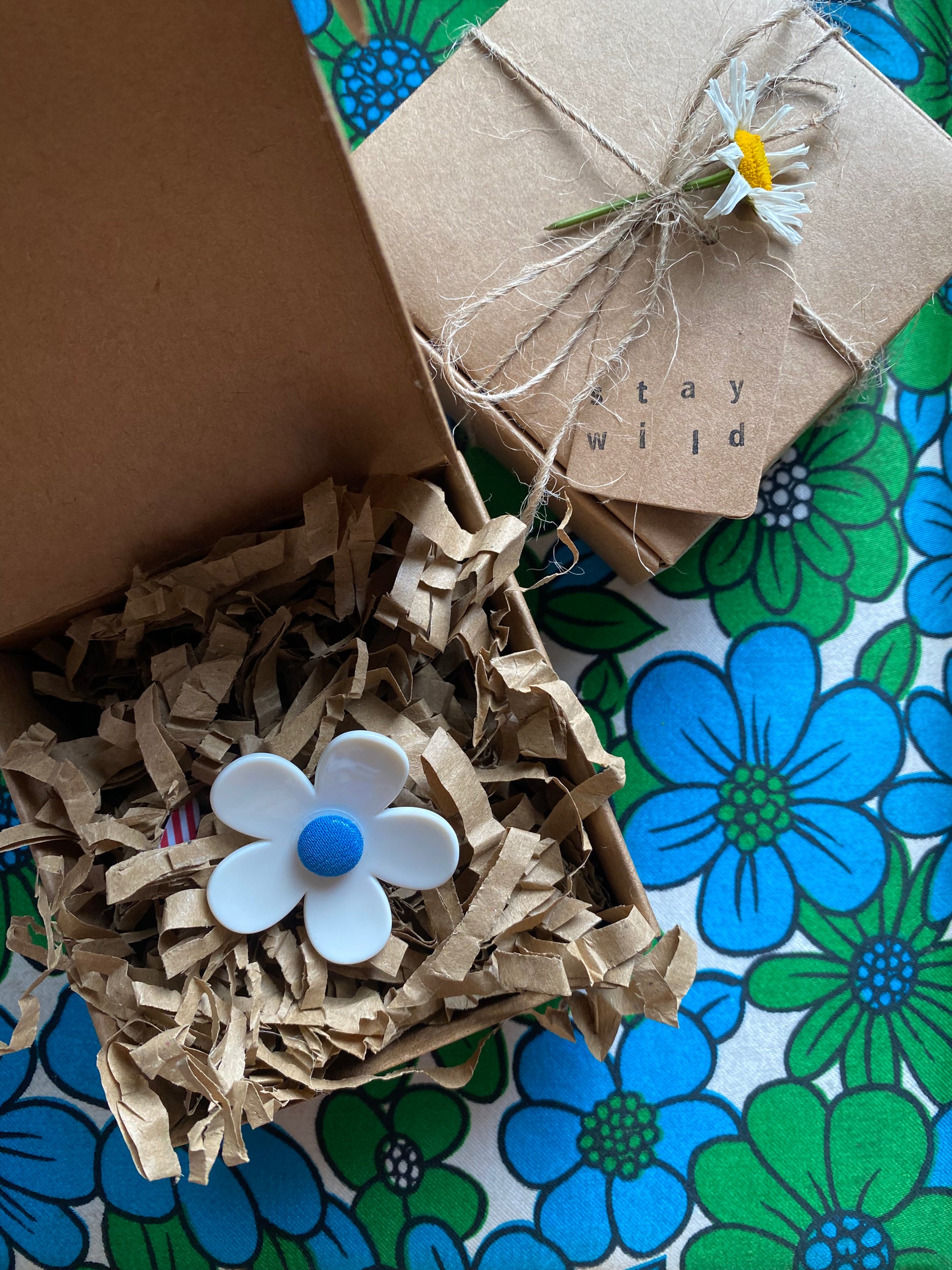 A handmade white daisy flower in a gift box on a floral-patterned surface