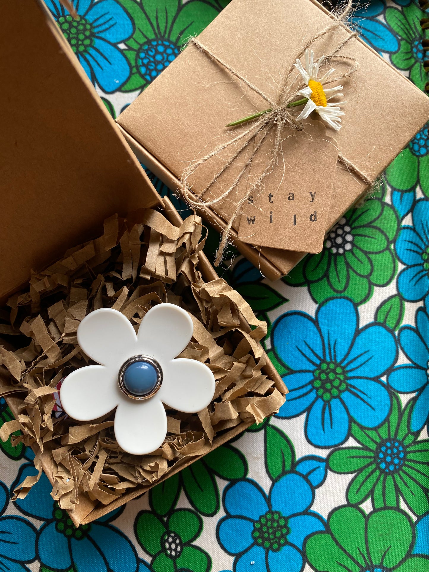 White daisy flower-shaped ring with a blue center on a floral-patterned surface