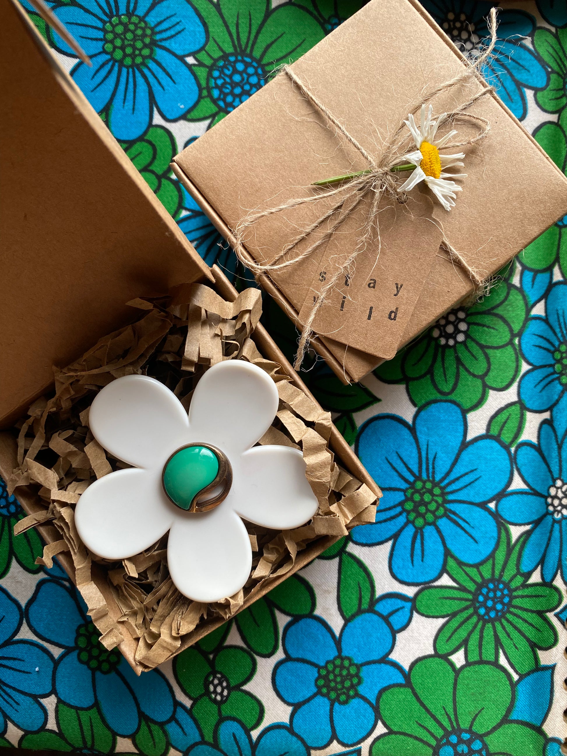 White daisy flower-shaped ring with green center on a floral-patterned surface