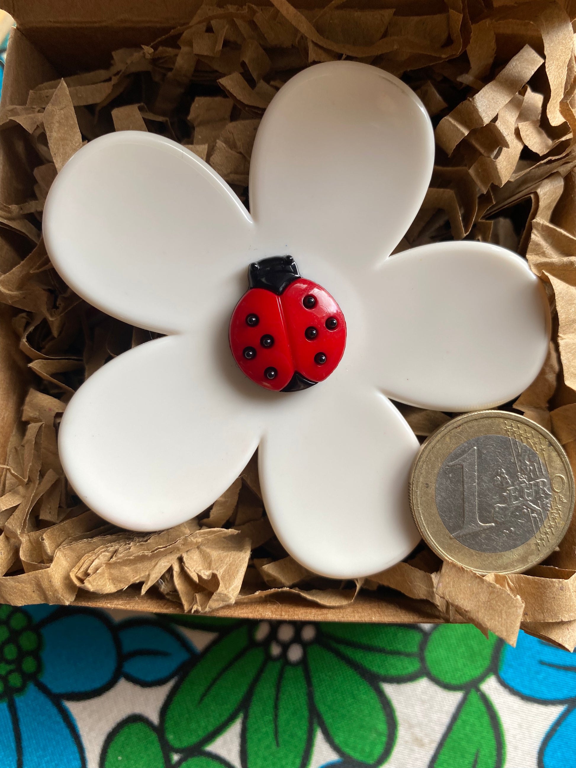 White up-cycled plastic daisy flower with a red ladybug in a box with brown tissue paper
