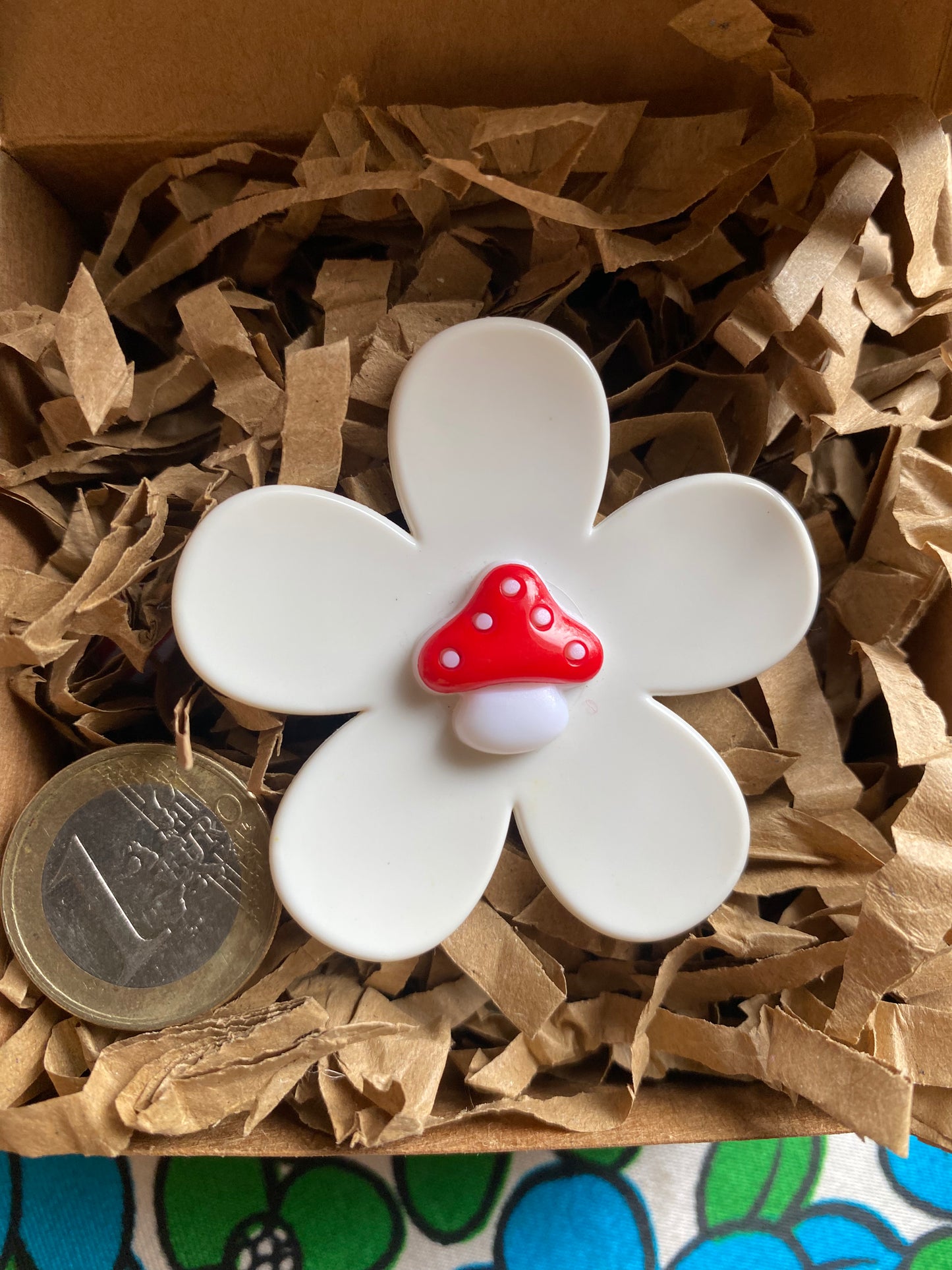 Handmade White daisy flower-shaped ring with a red mushroom on top, placed on brown paper gift box