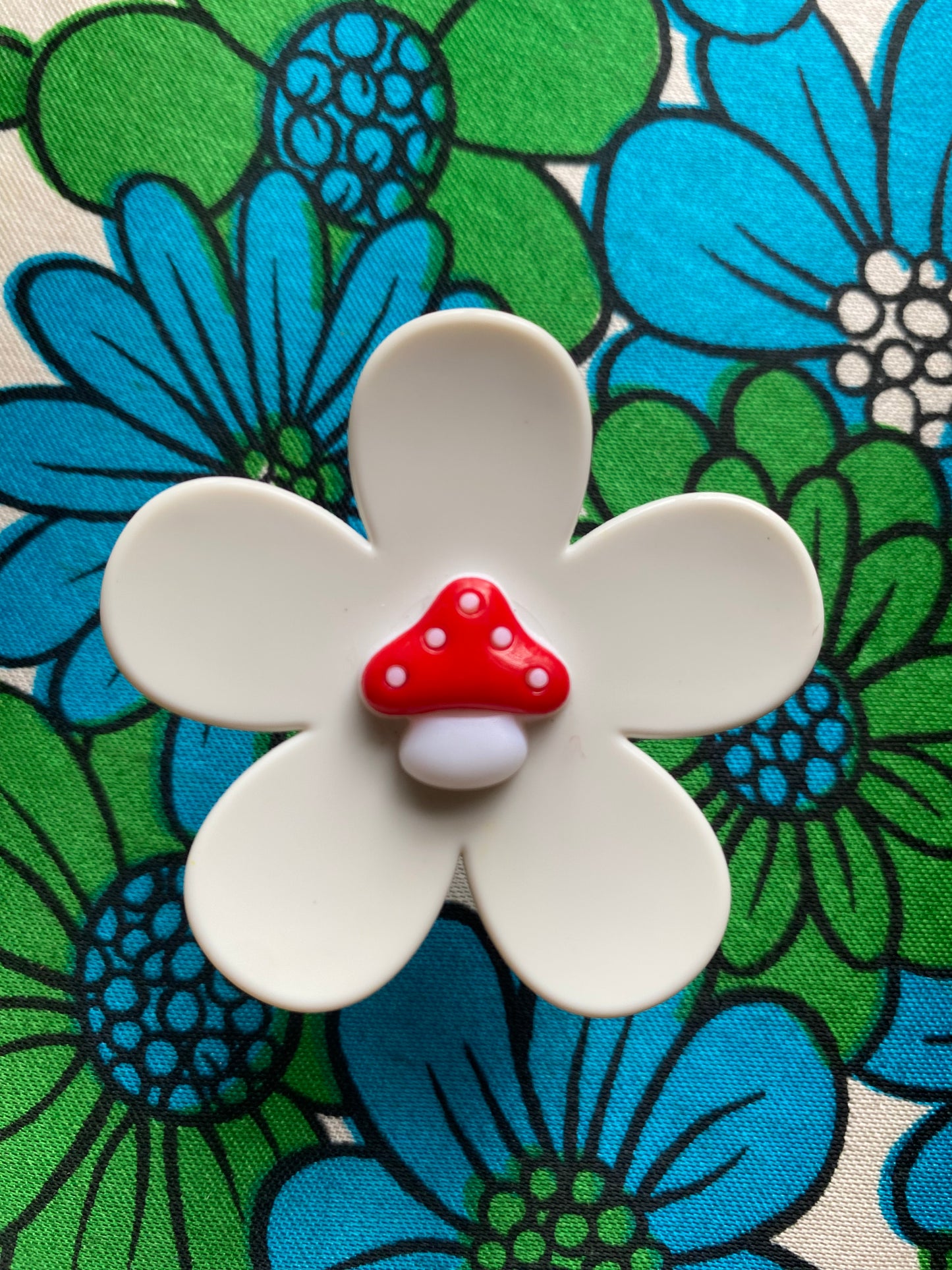 Handmade White daisy flower-shaped ring with a red mushroom cap in the center on a floral background
