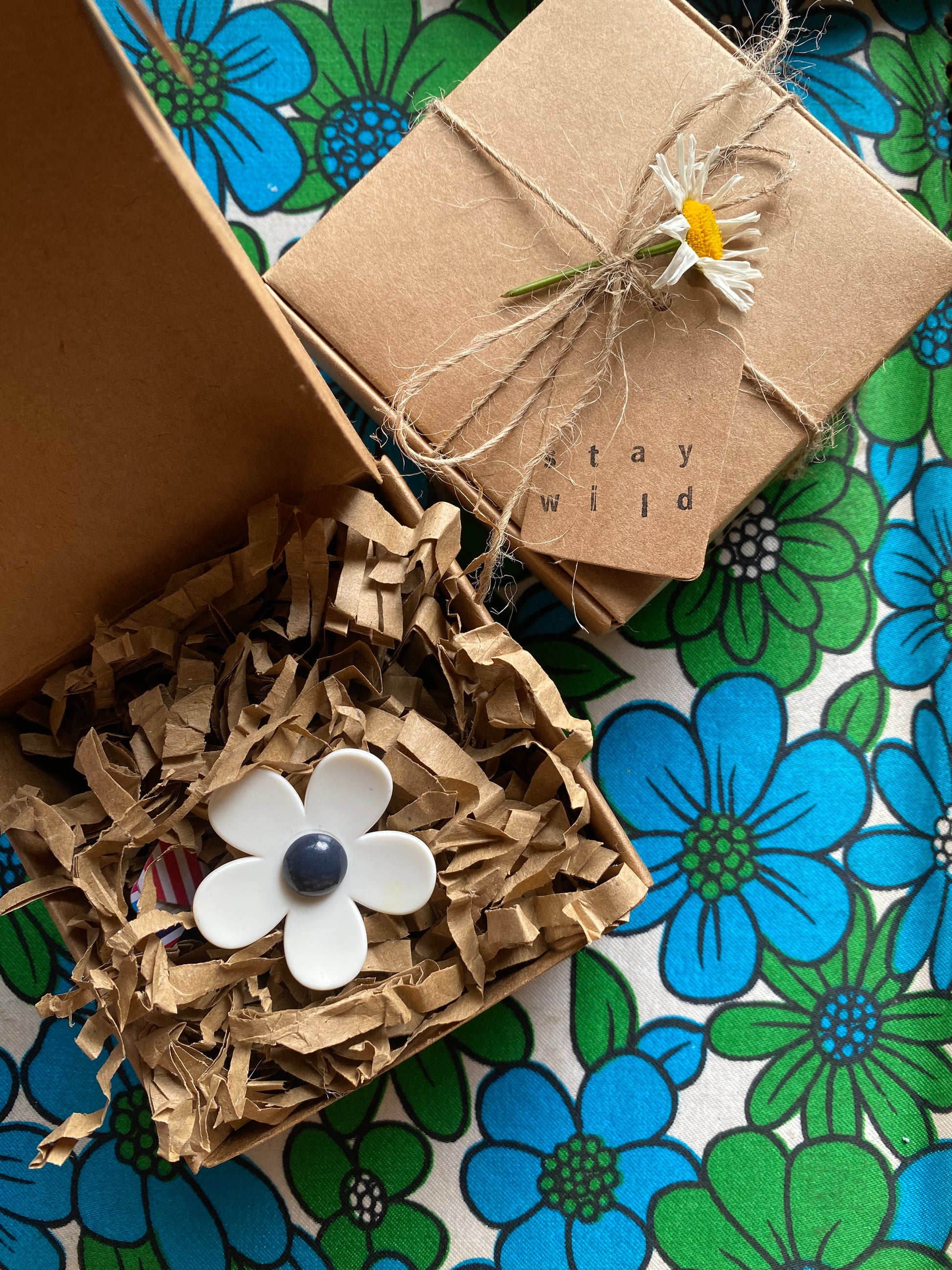 Gift box with decorative flower on a floral-patterned surface with a handmade daisy ring inside 