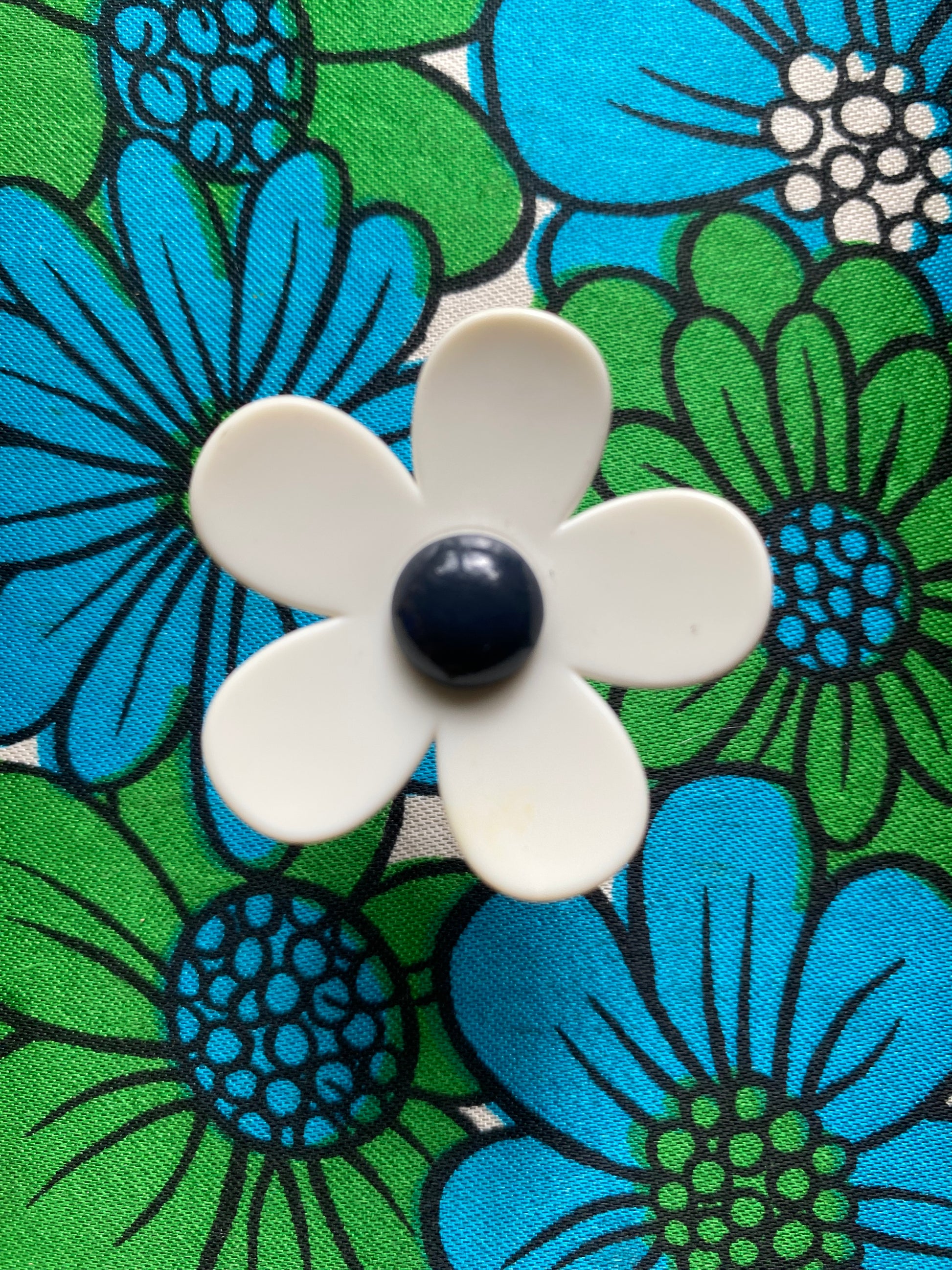 Handmade white daisy flower-shaped ring with a navy center on a floral patterned background