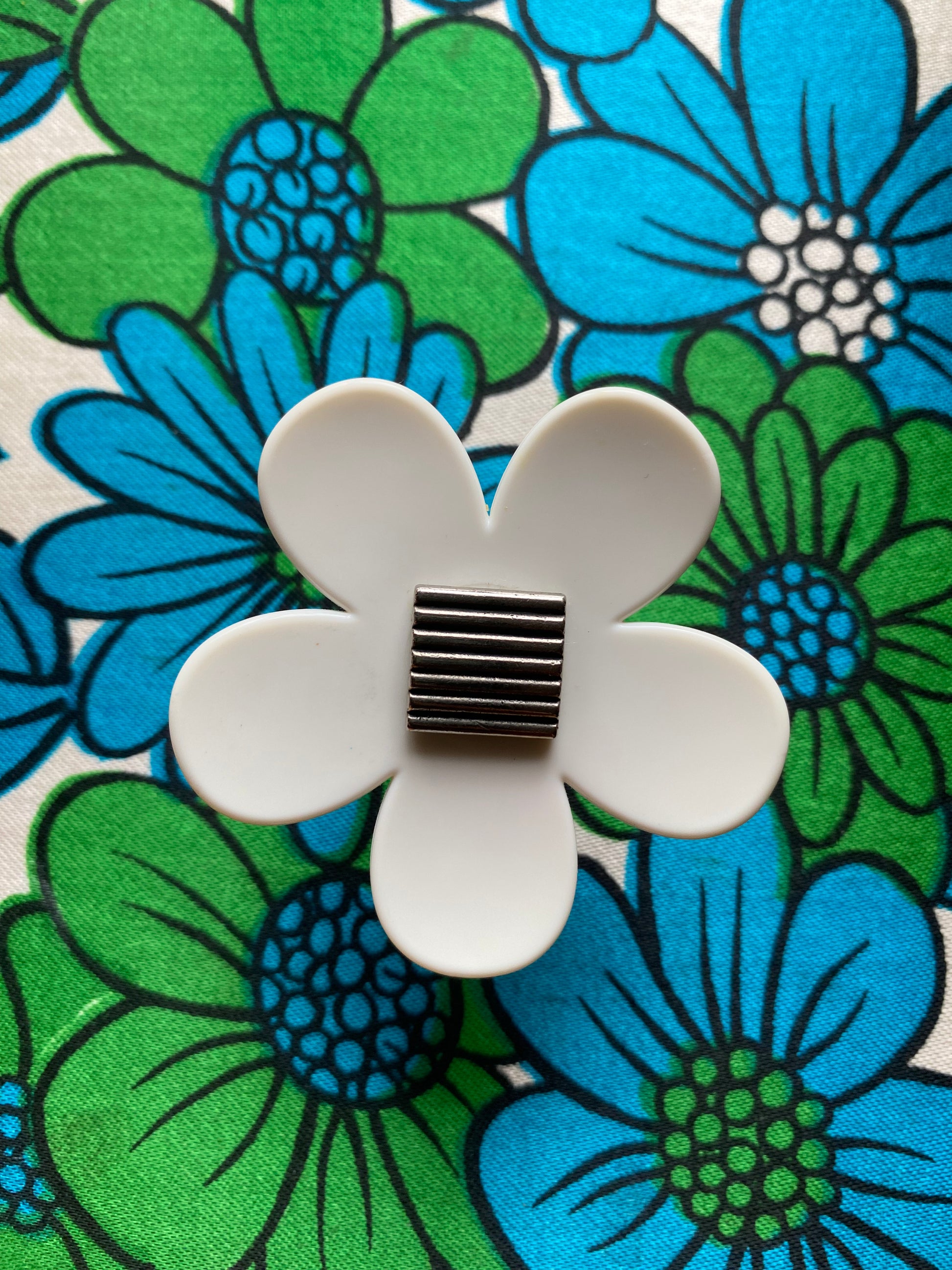 Handmade upcycled White daisy flower-shaped ring displaying on a floral background with blue and green flowers
