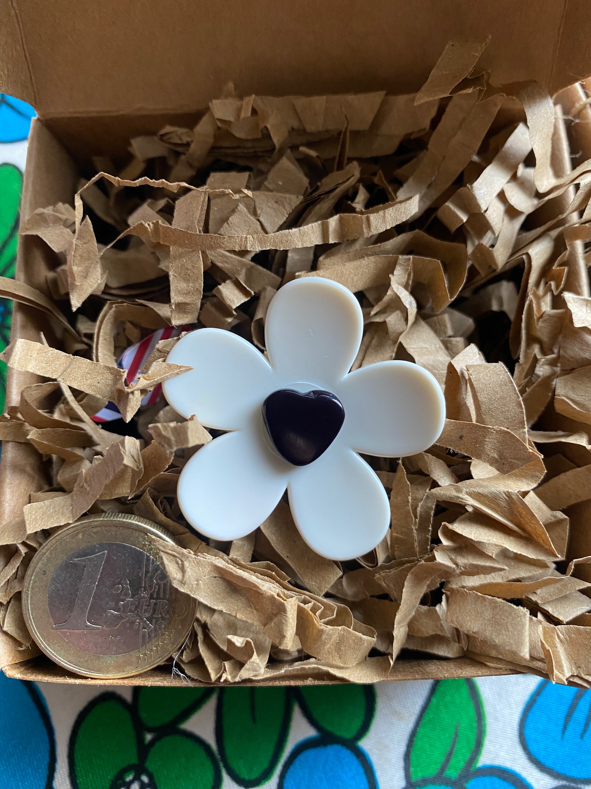 Handmade daisy white flower-shaped ring with a black center on a eco friendly brown paper inside a gift  box.
