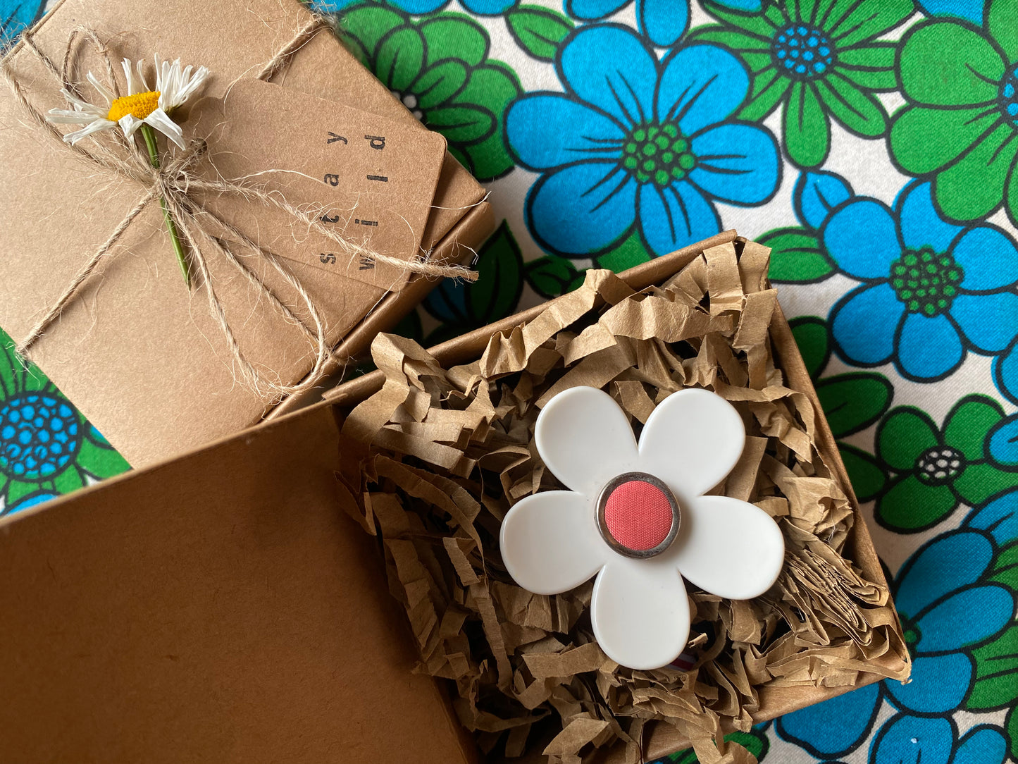 Handmade daisy white flower ring and pink center on brown paper against a floral-patterned background