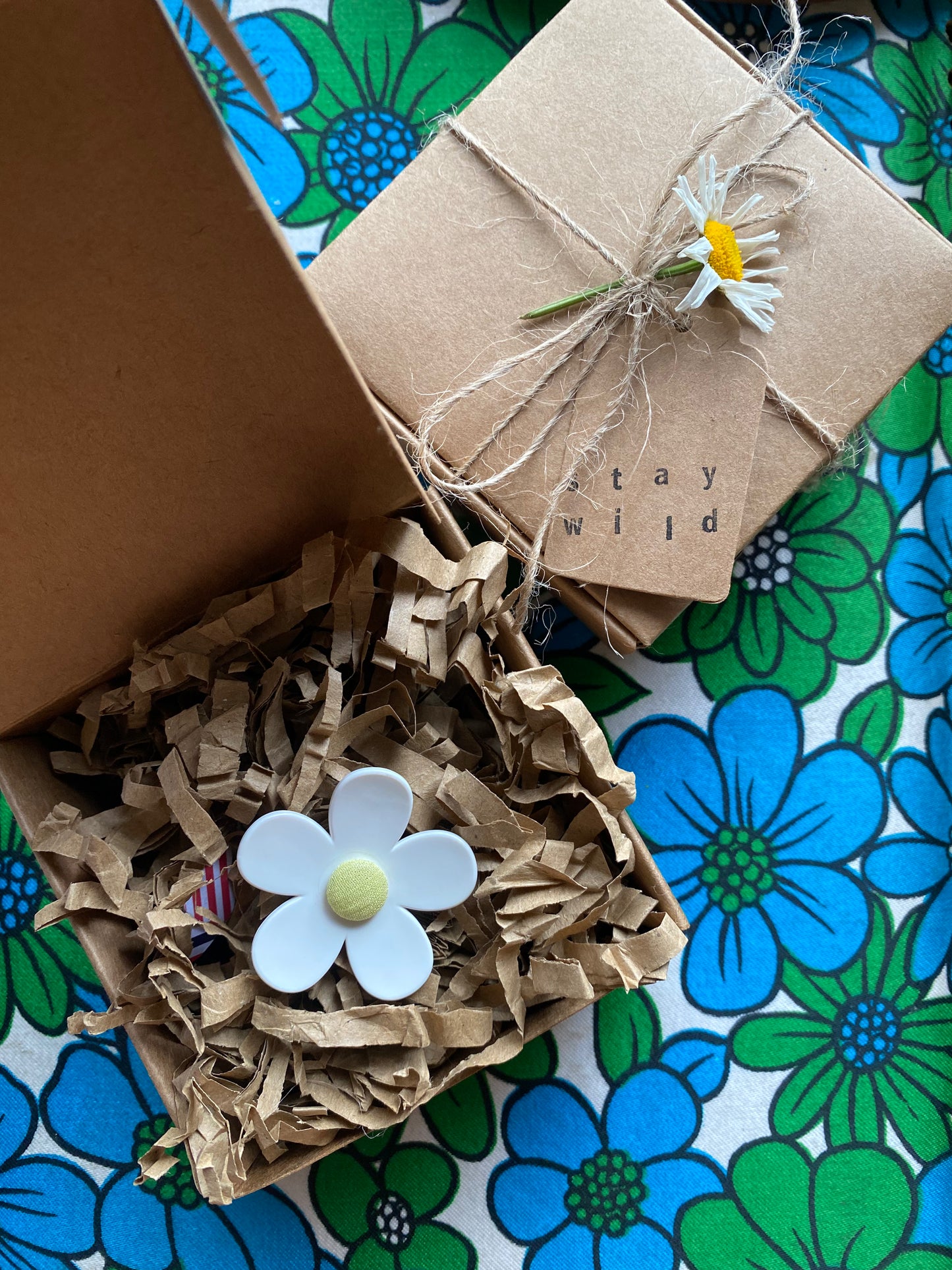 Gift box with decorative paper and a 'stay wild' tag on a floral-patterned surface.