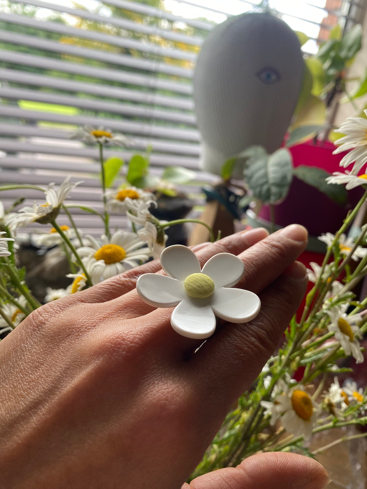 Hand modeling a handmade daisy flower ring with a blurred garden background